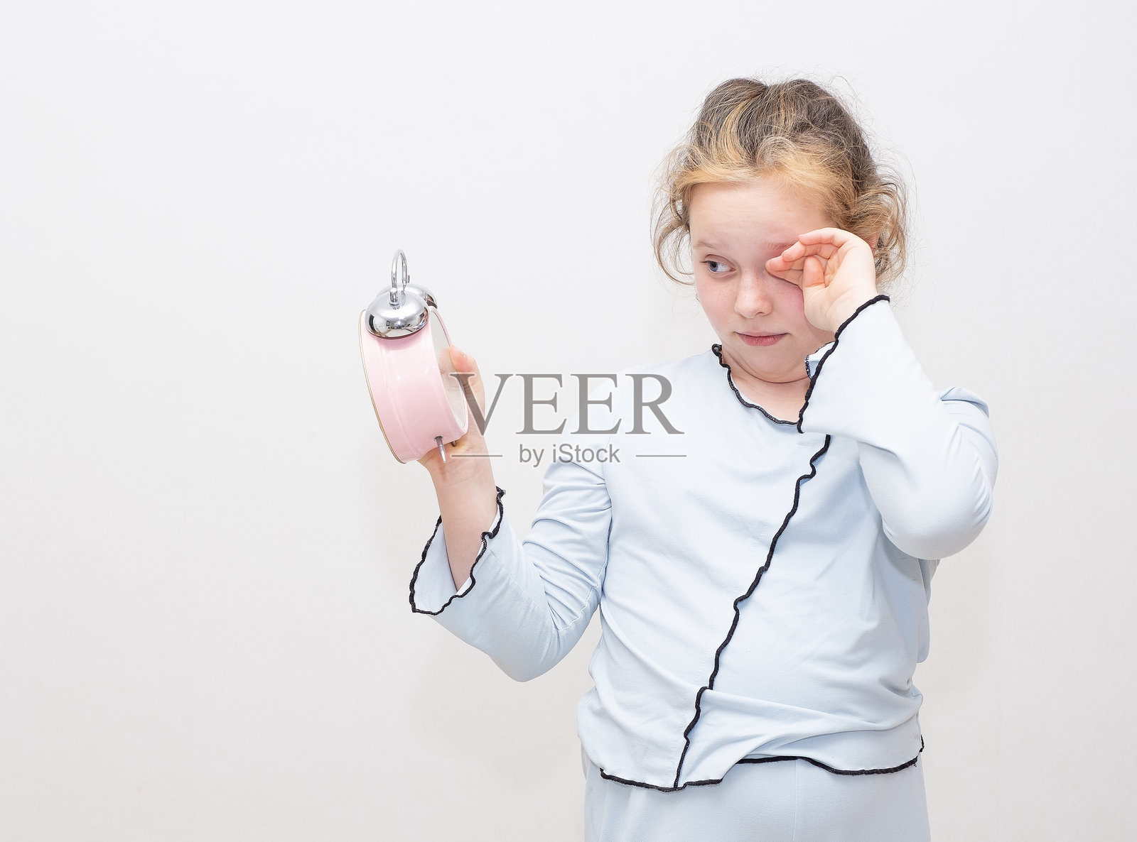 白人女孩，孩子，想要睡觉，揉着眼睛。女孩手里拿着一个闹钟。照片摄影图片