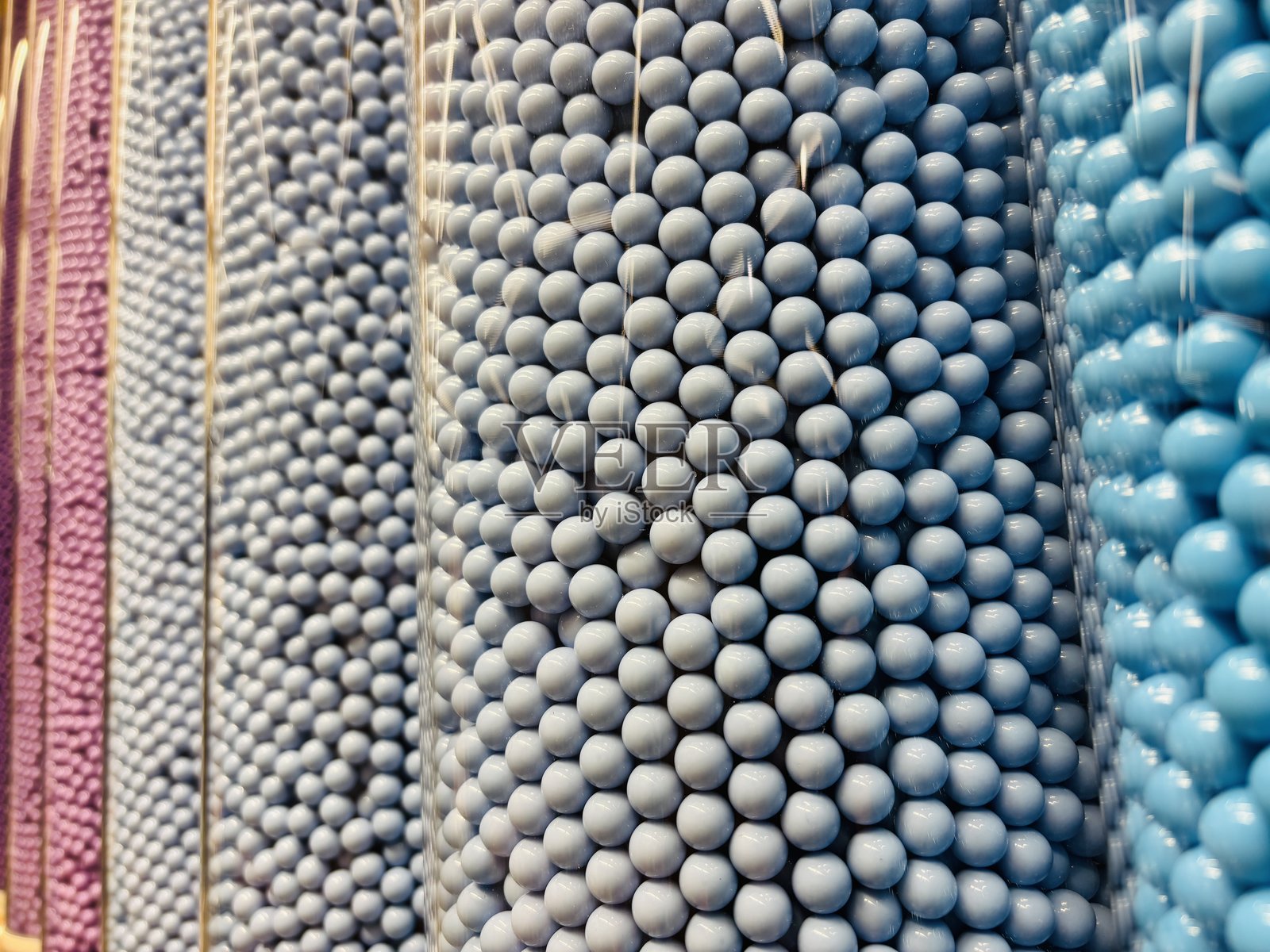 五颜六色的糖衣巧克力球在高透明圆柱中排列，展示出紫色、灰色和蓝色的色调。照片摄影图片