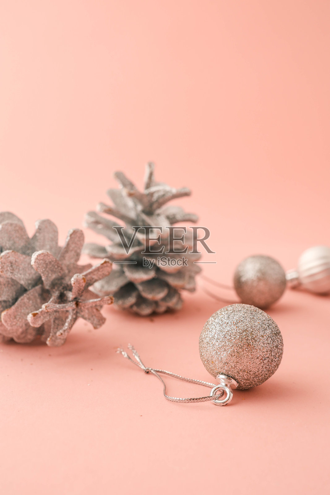 银色闪光的松果和圣诞装饰品特写，排列在粉色背景上。非常适合节日、假日和极简风格的季节性设计或广告。照片摄影图片