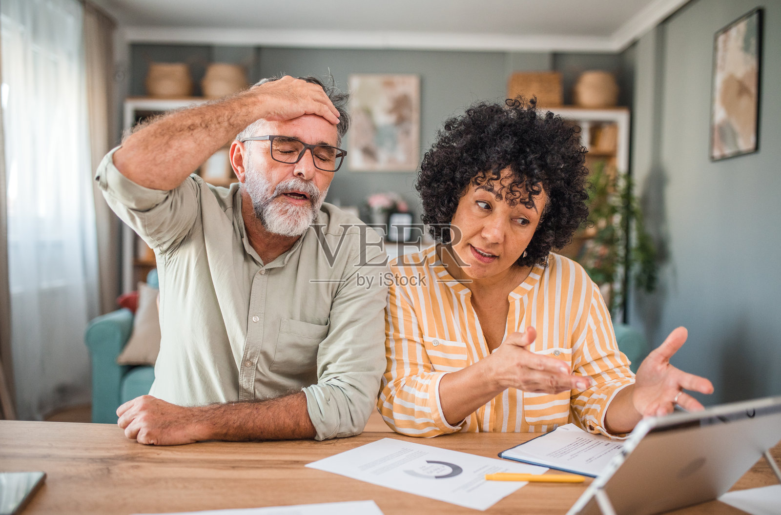 担忧的中年夫妇坐在餐桌旁，通过数字平板查看水电账单。关心的男女账户里没有足够的钱。照片摄影图片