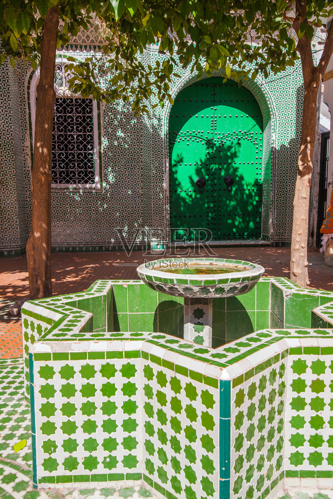 一个宁静的庭院，设有瓷砖喷泉、郁郁葱葱的树木和一扇生机勃勃的绿色门，营造出一个带有传统建筑细节的和平绿洲。照片摄影图片