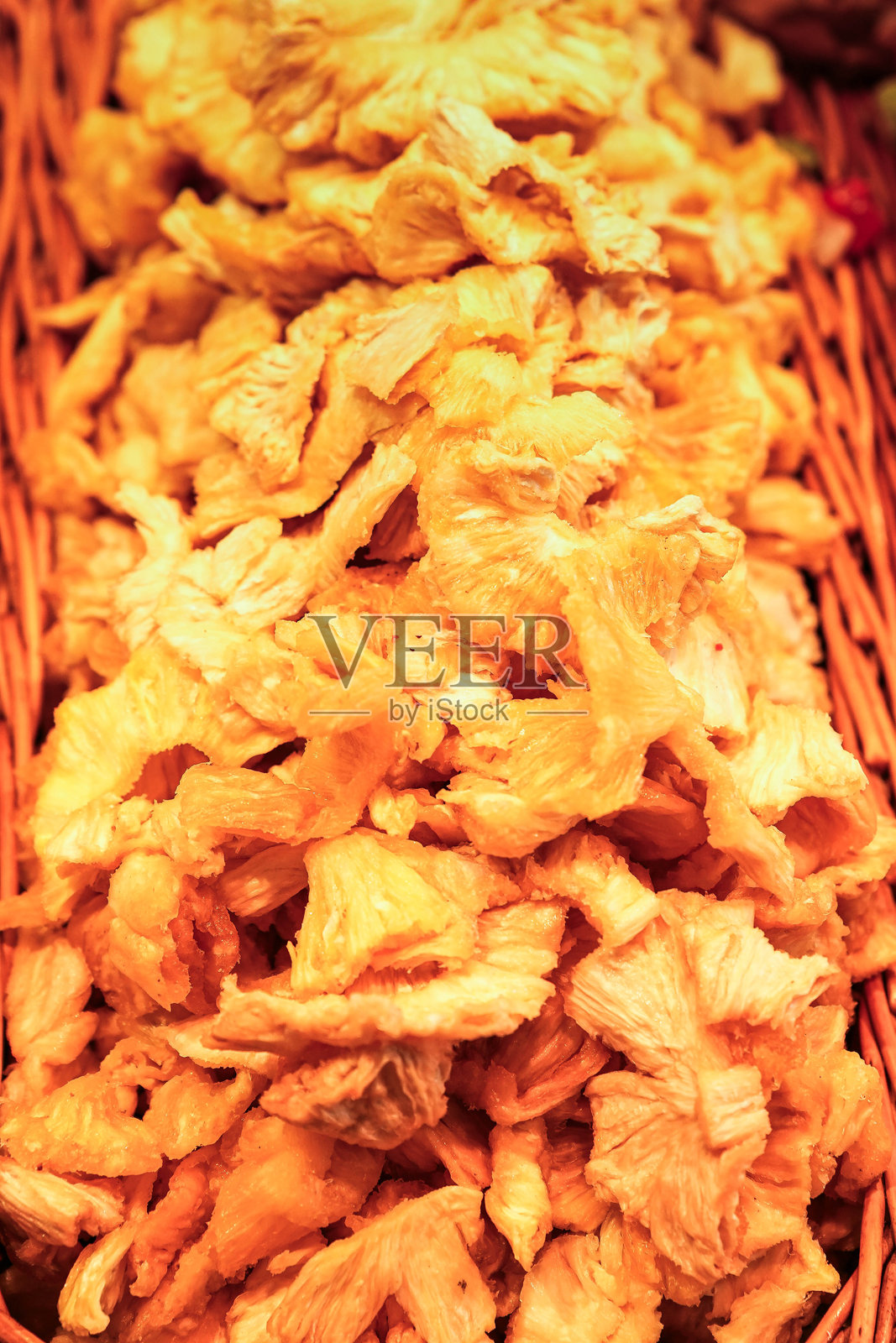 一堆色泽鲜艳、口感 chewy 的甜干菠萝，展示在一个乡村风格的篮子里，适合作为健康零食或美味食谱的配料。照片摄影图片