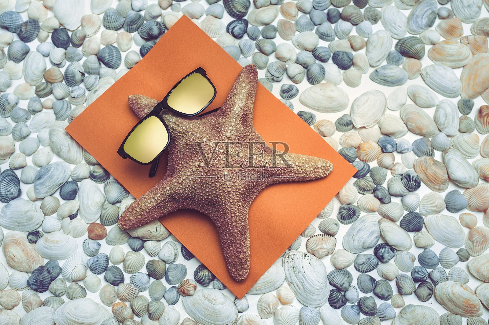 一只搞笑的棕色海星（名人）戴着太阳镜，躺在贝壳上的毛巾上晒太阳。夏季假期、旅行和旅游的概念。俯视图。照片摄影图片