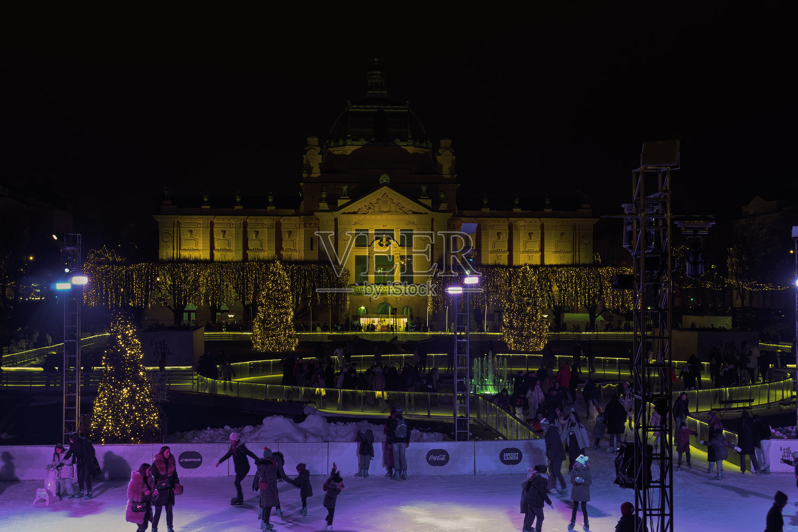 克罗地亚萨格勒布的Ledeni Park滑冰场,节日装饰环绕,夜晚艺术画廊的建筑灯光璀璨。照片摄影图片
