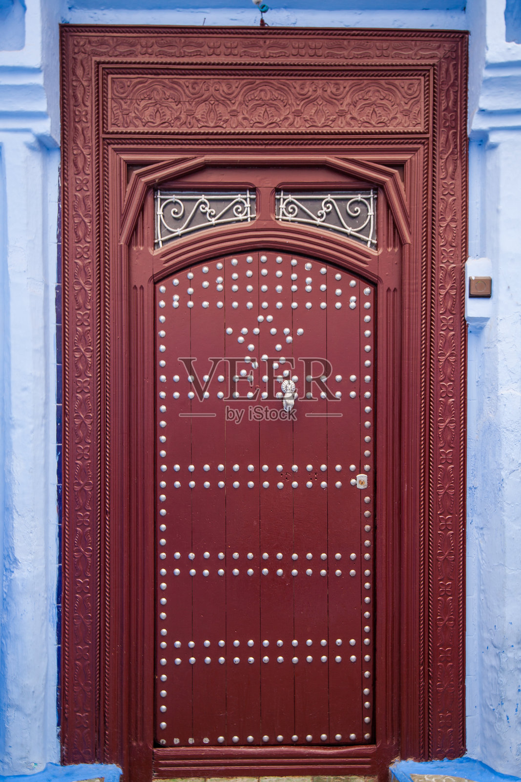 装饰华丽的深红色木门，带有精美的雕刻和金属钉，背景是对比鲜明的蓝色墙壁照片摄影图片
