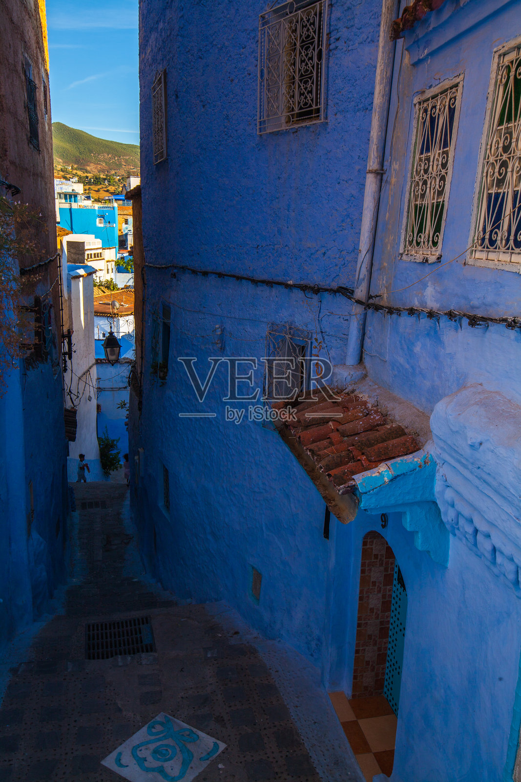 狭窄的下坡街道，位于一个蓝色涂装的小镇，远处可见建筑和山丘的轮廓照片摄影图片