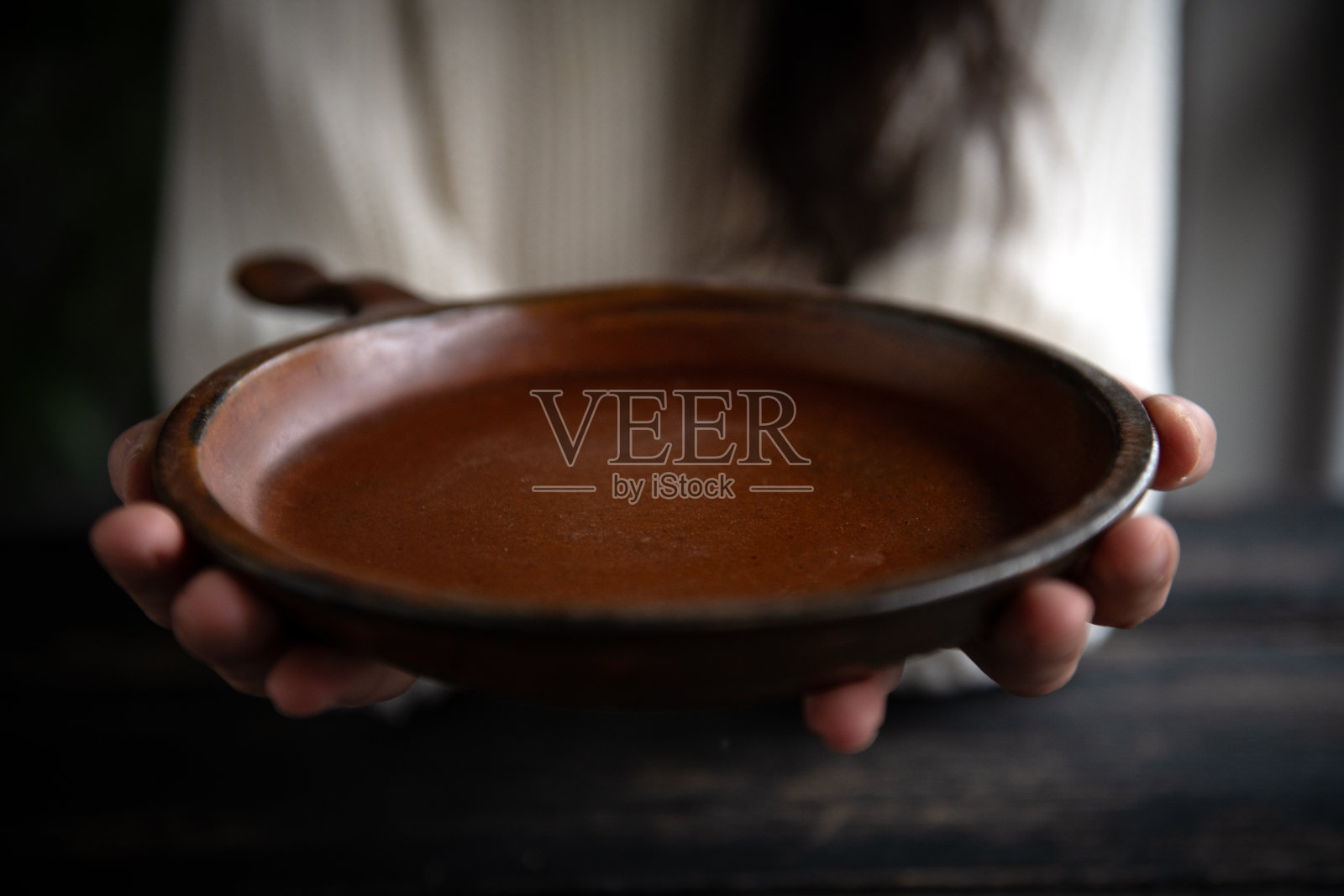 女人双手托着一个盘子，背景是深色木材。照片摄影图片