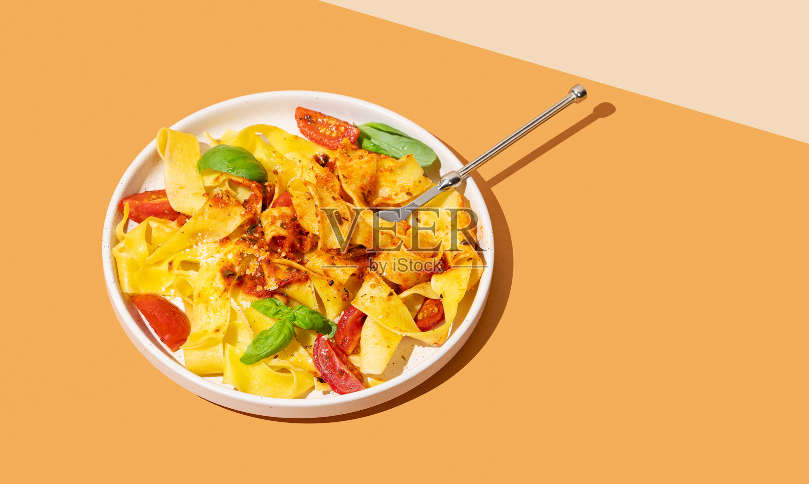 橙色背景上，盘子里盛着意大利宽面条或帕帕尔德尔面条，配有番茄酱、罗勒和帕尔马干酪，旁边放着叉子。照片摄影图片