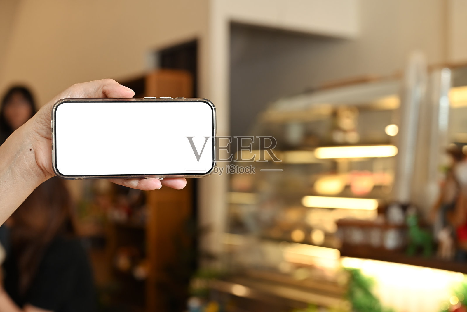 在温暖灯光的咖啡馆里，手握着横屏的智能手机，屏幕为空白。照片摄影图片