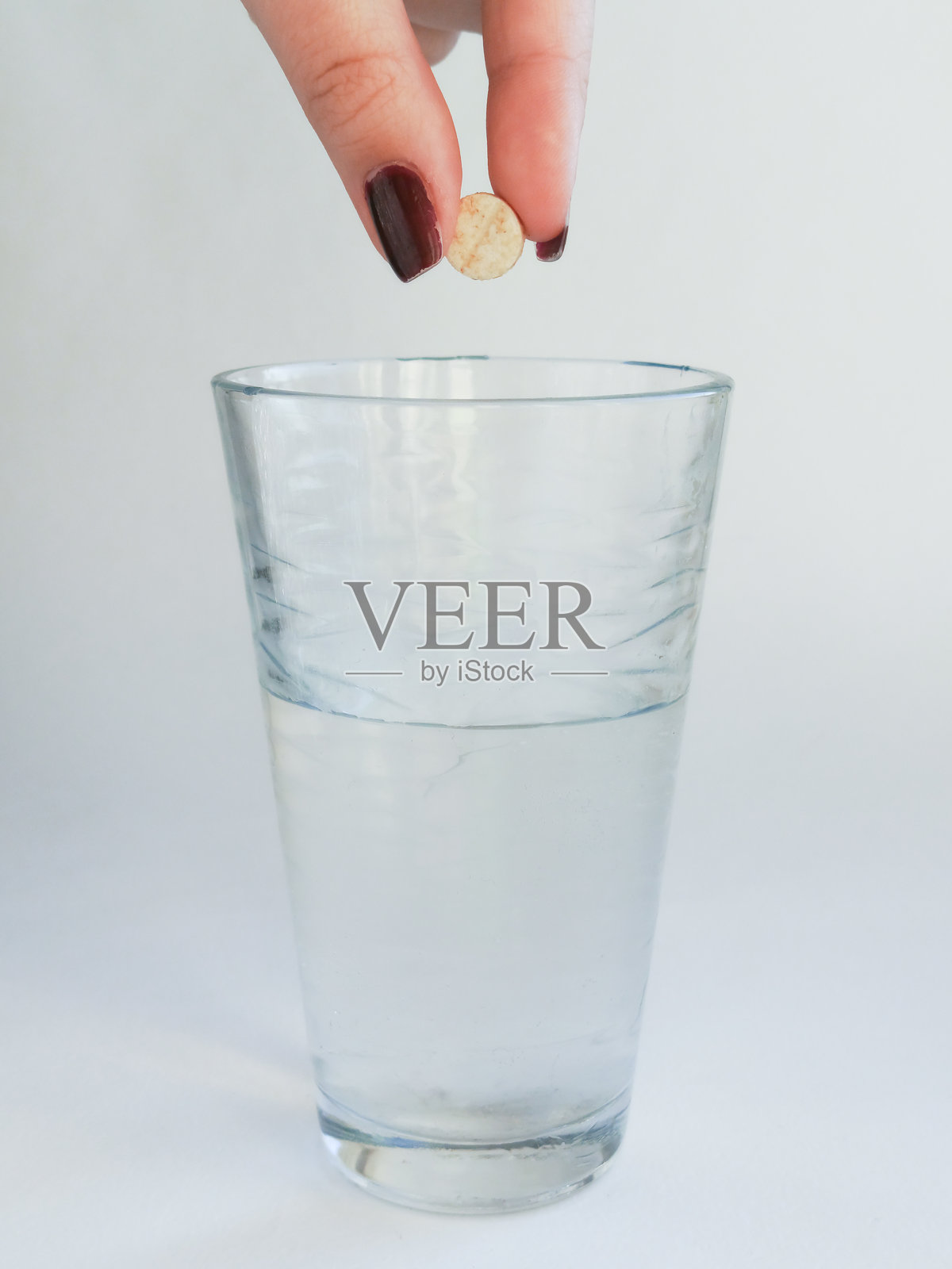 一只女性的手握着一颗圆形白色药片，悬在一杯水上方。水溶性药片。喉咙痛的药物。抗抑郁药。药物的副作用。照片摄影图片