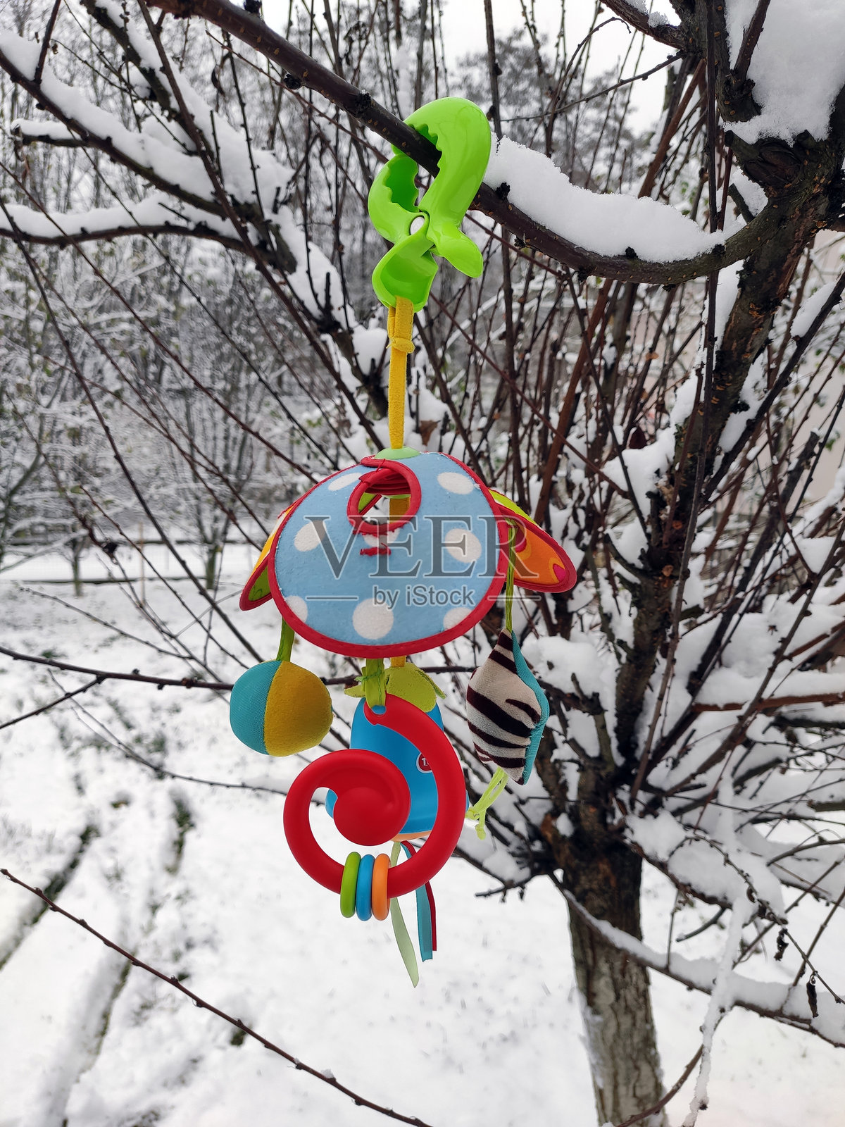 儿童玩具吊坠，形状像伞，色彩鲜艳，悬挂在被雪覆盖的树枝上。背景是冬季风景，雪覆盖的树木和洁白的松软雪。红色、绿色、蓝色、靛蓝和黄色，具有不同的纹理。照片摄影图片