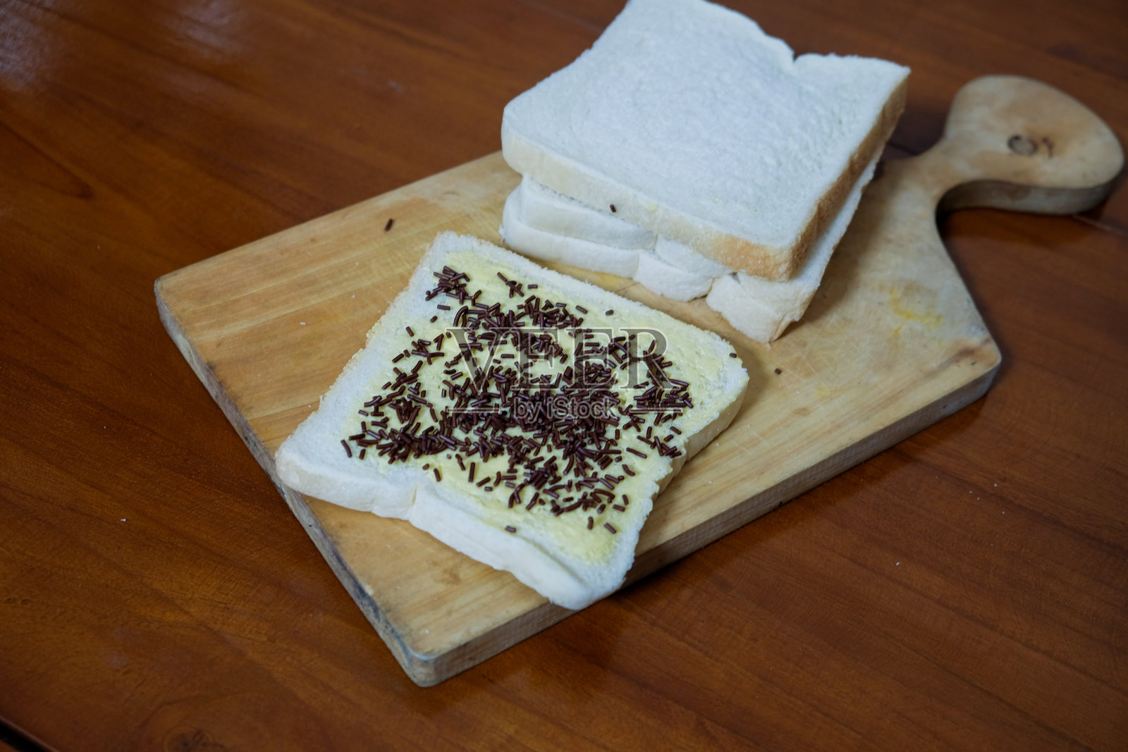 早餐用黄油涂抹的三明治面包，上面撒有巧克力糖屑，放在木质切菜板上，背景是木桌。照片摄影图片