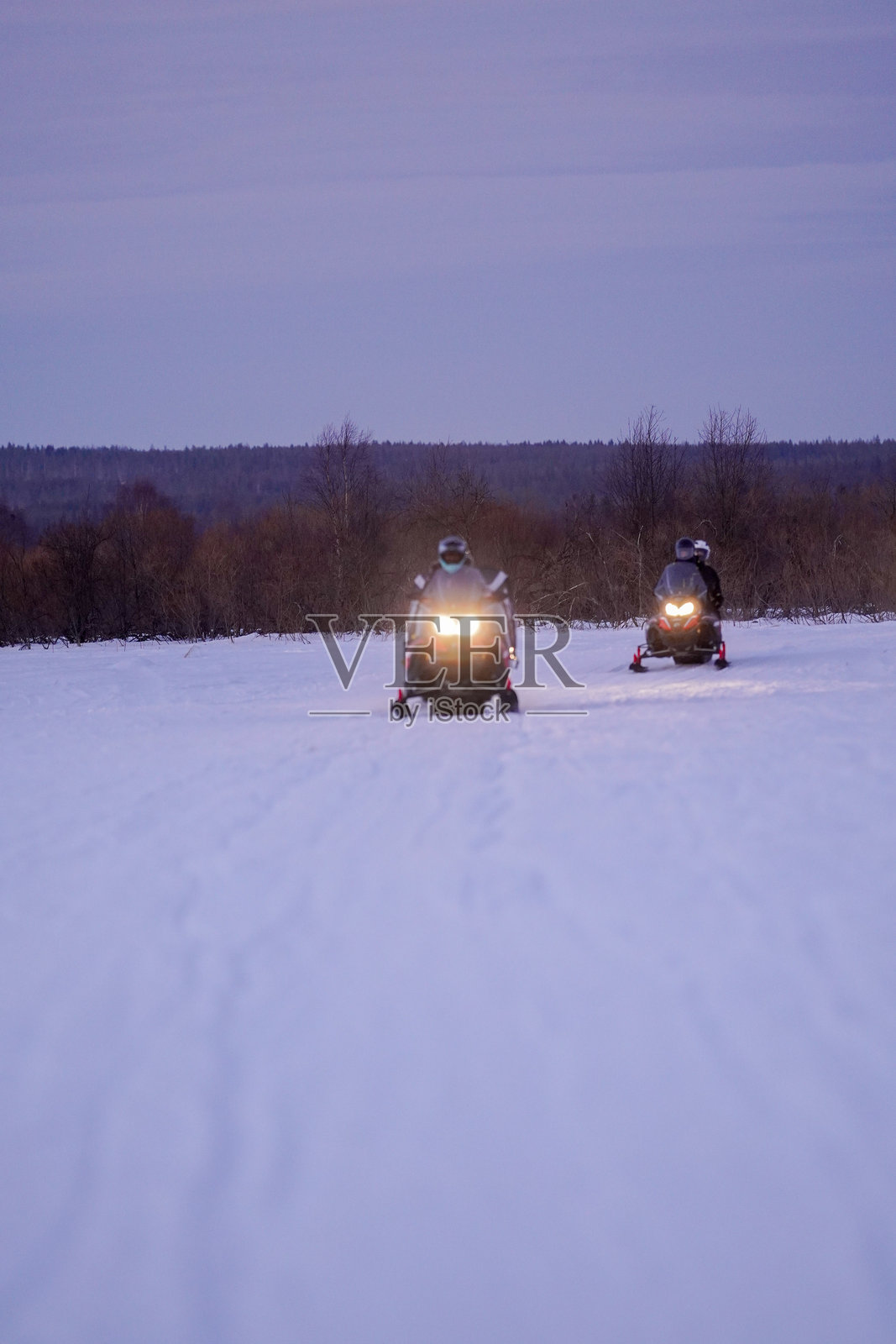 雪地摩托骑行者在黄昏时分穿越冬季风景照片摄影图片