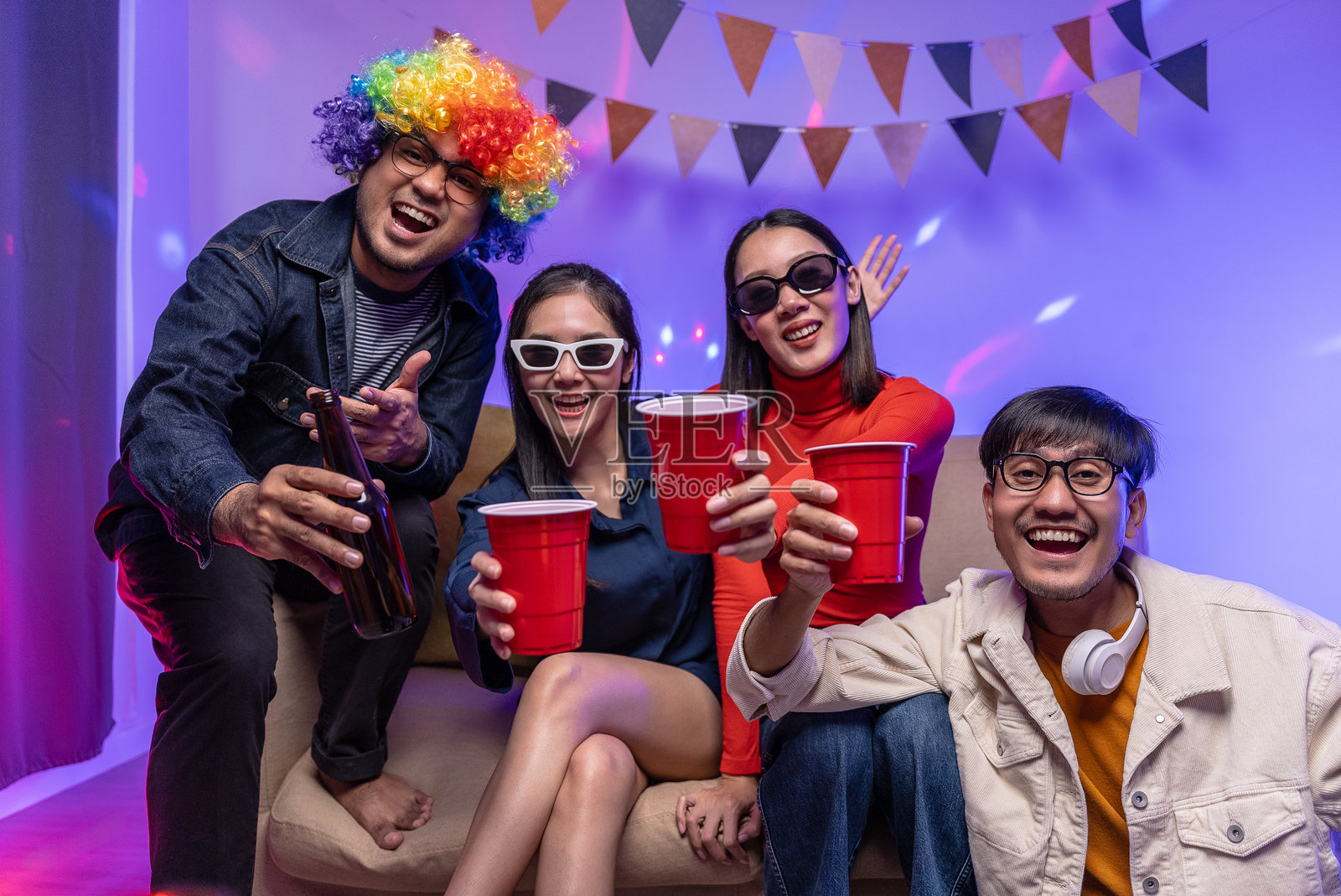 快乐的亚洲多元化朋友们在聚会上庆祝，举着啤酒瓶碰杯。家中聚会的朋友们一起享受欢乐时光，尽情舞蹈。新年派对的概念。照片摄影图片