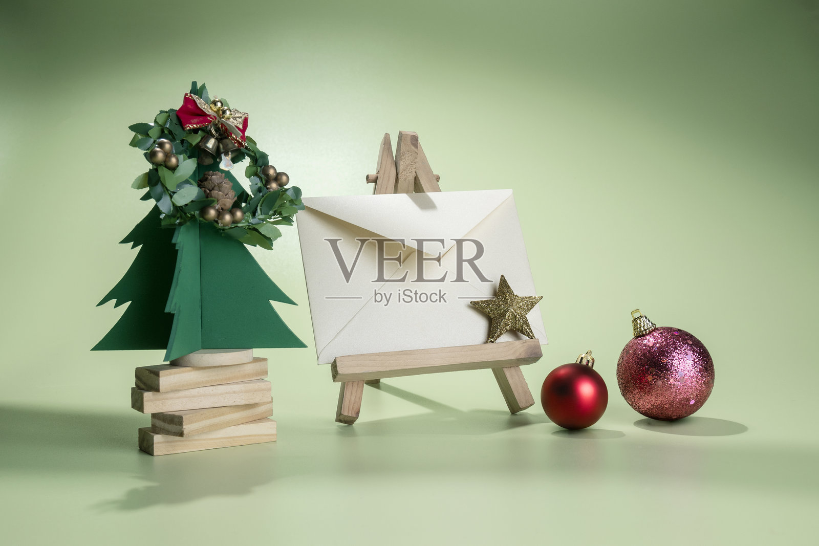 圣诞树迷你模型和圣诞装饰品的特写，旁边有一个信封，放在木制画架上，背景为彩色。照片摄影图片