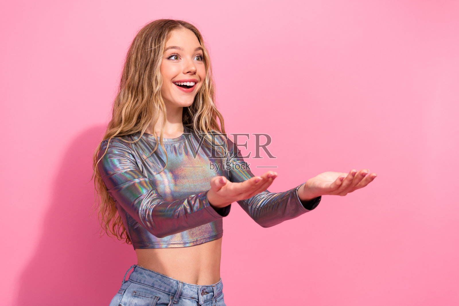 穿着闪亮上衣的时尚年轻女性在粉色背景下兴奋地张开双手照片摄影图片