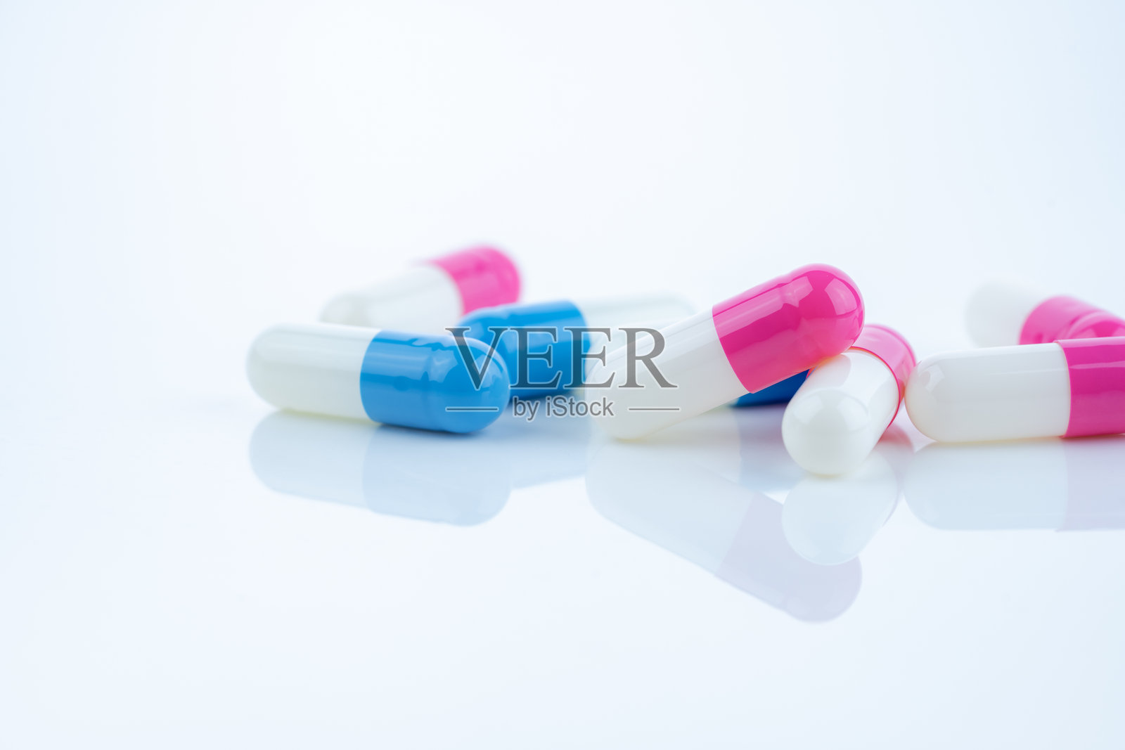 蓝色和粉色的胶囊药丸散落在白色背景上，展示了药品、医疗概念以及处方药在促进治疗和患者健康中的作用。照片摄影图片