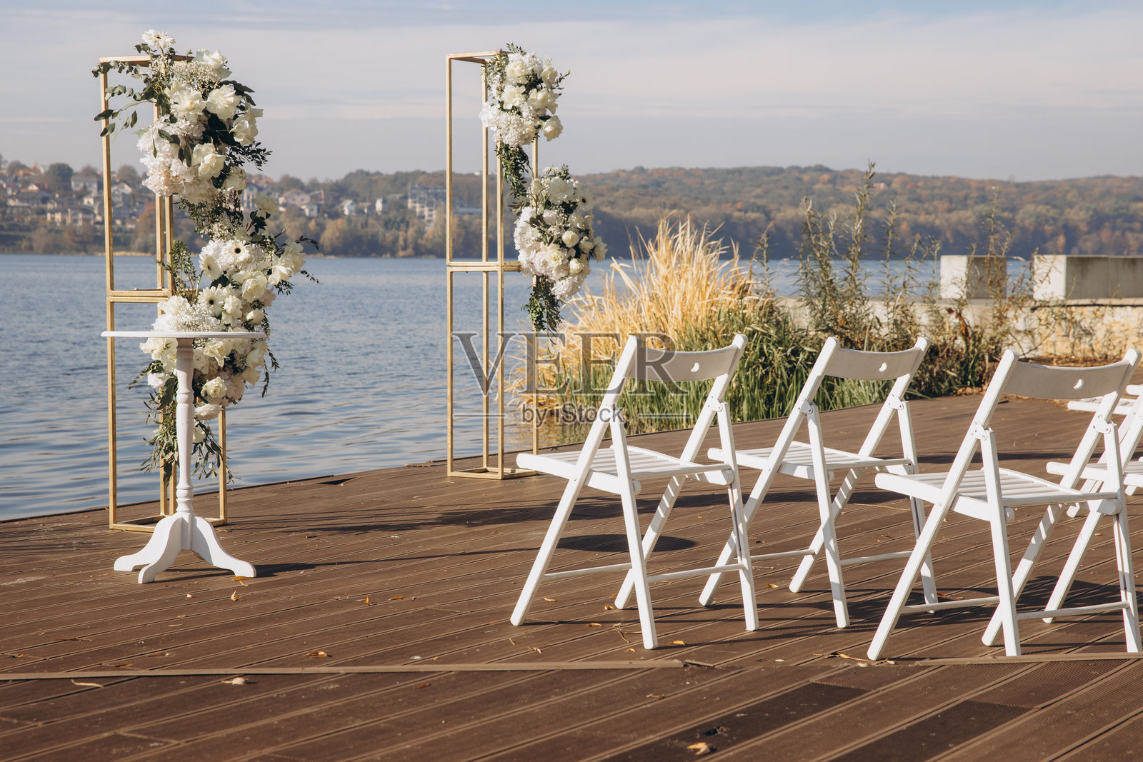 湖边木栈道上的婚礼仪式布置，白色椅子和花卉装饰。照片摄影图片