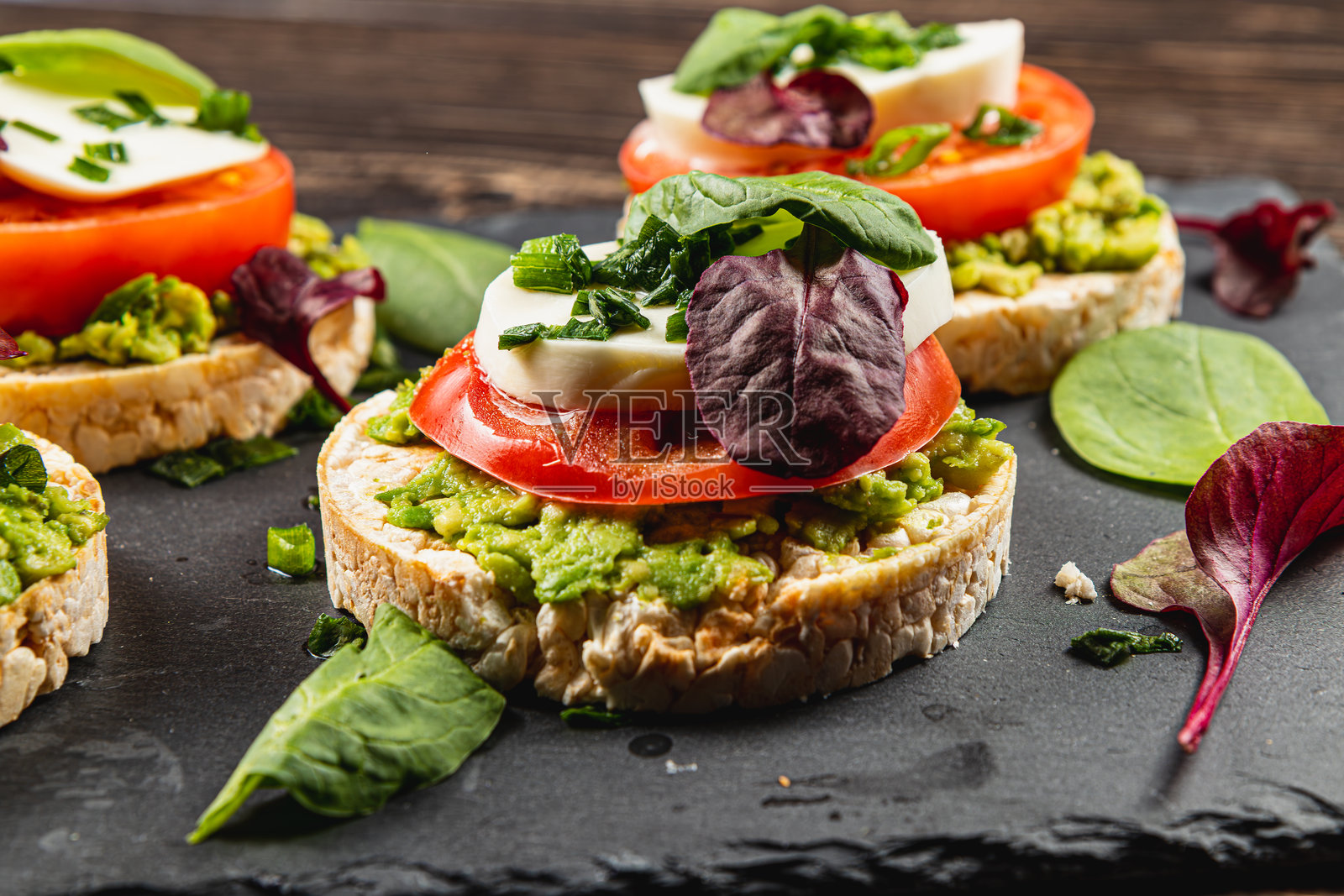 石头上放着米饼，上面有马苏里拉奶酪、鳄梨、菠菜和洋葱，旁边是一张木桌。照片摄影图片