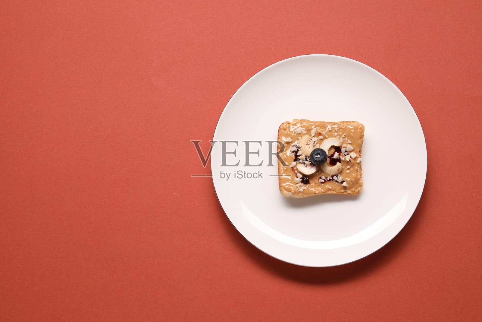 美味的坚果黄油、蓝莓和腰果涂抹在珊瑚色背景上的吐司，俯视图。留有文字空间。照片摄影图片