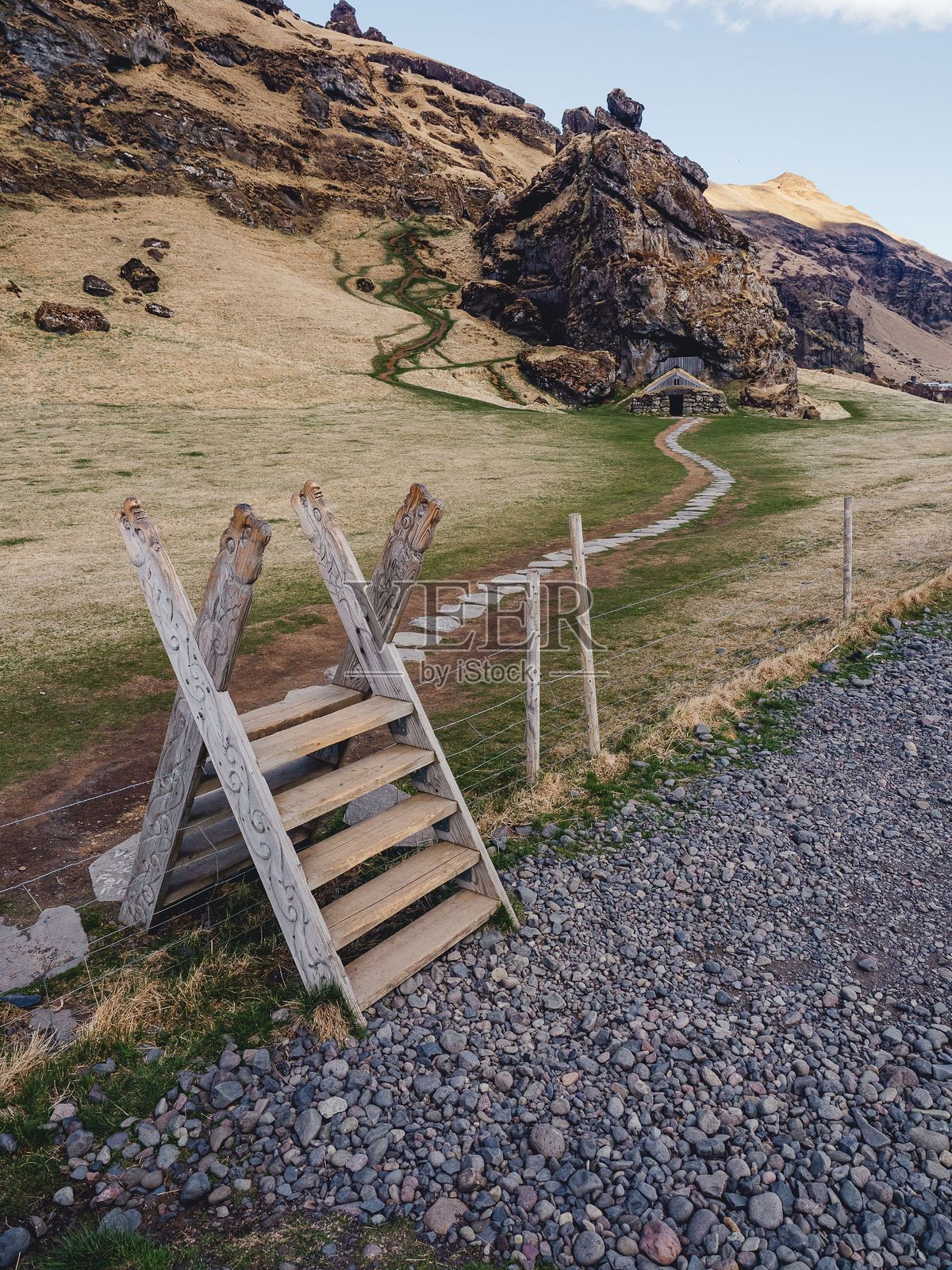 乡村风格的木栅栏横跨在通往小山坡和小洞穴居所的岩石小径上。照片摄影图片