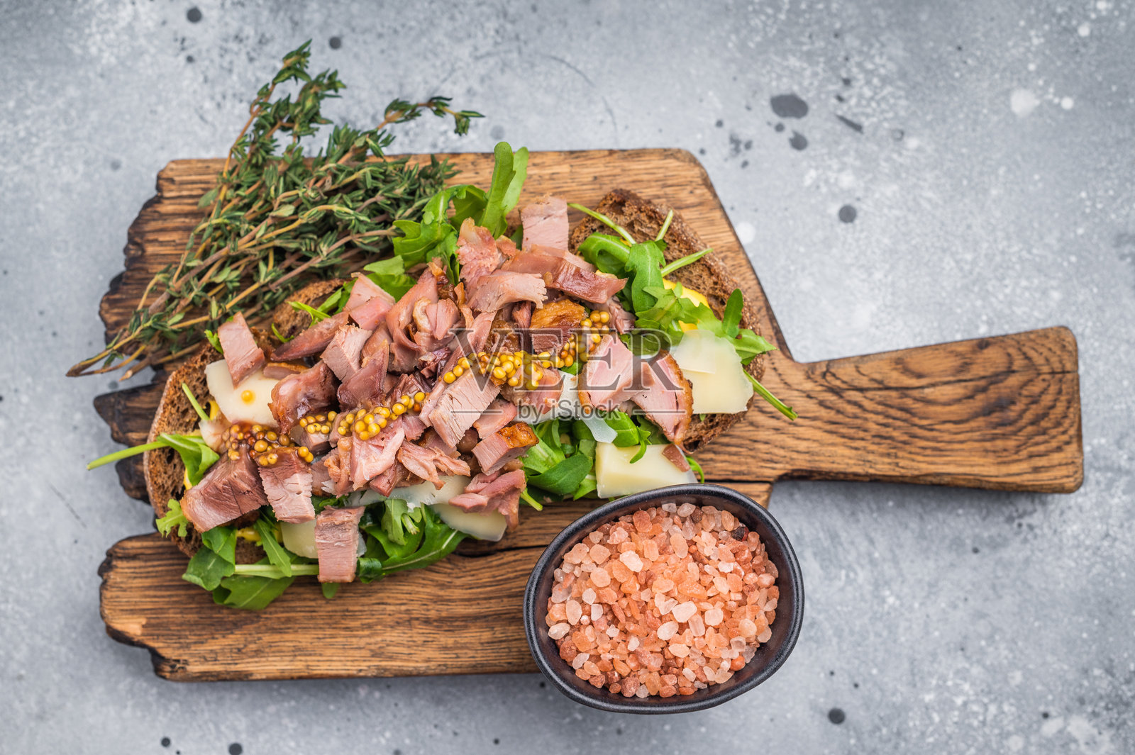 带有鸭肉片、鹅肝、芝麻菜和奶酪的开放式三明治，放在木板上。灰色背景。俯视图。照片摄影图片