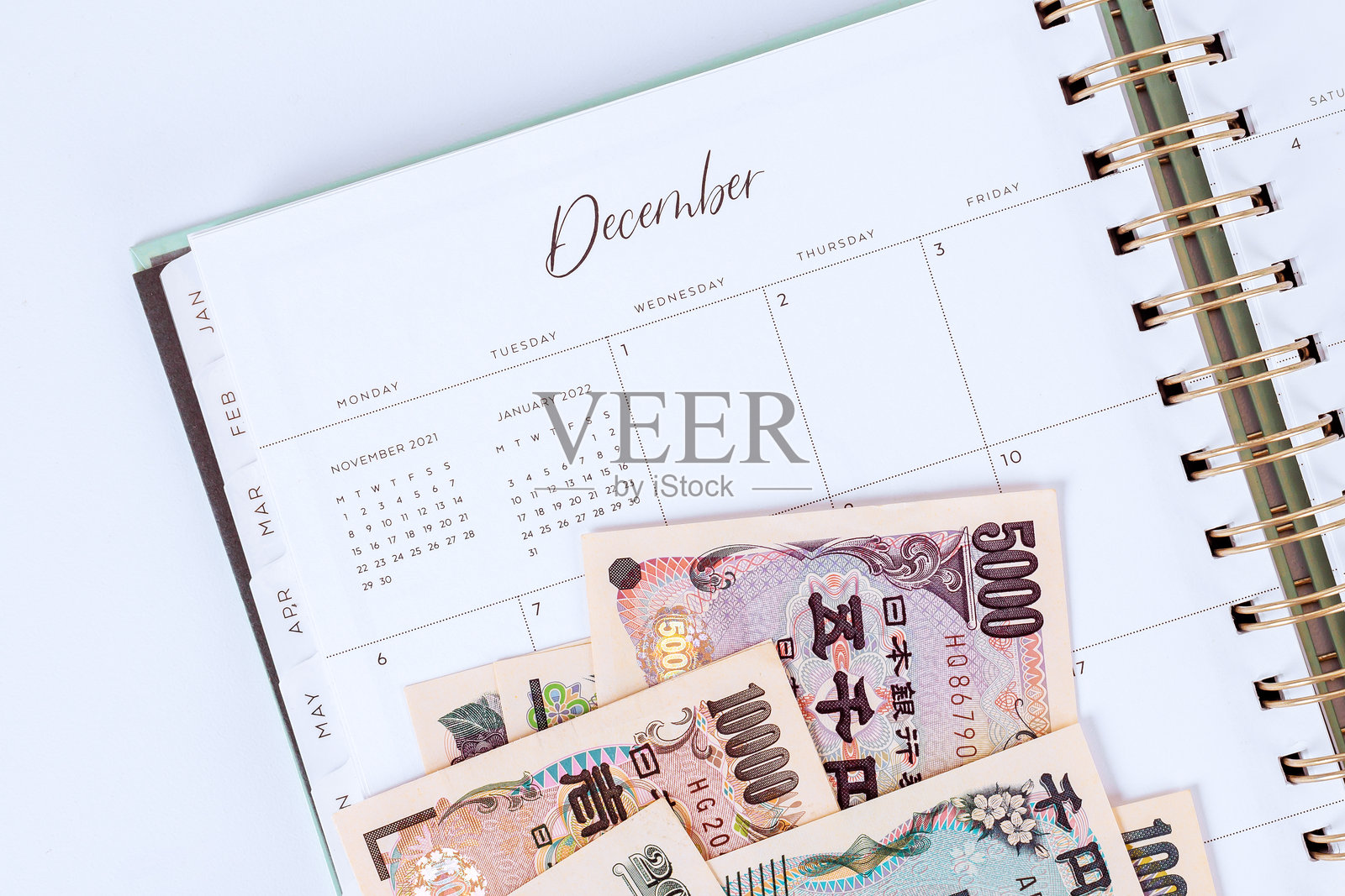 螺旋装订的日历显示十二月的开始，上面放着日元，场景传达出财务准备和费用跟踪的感觉。照片摄影图片