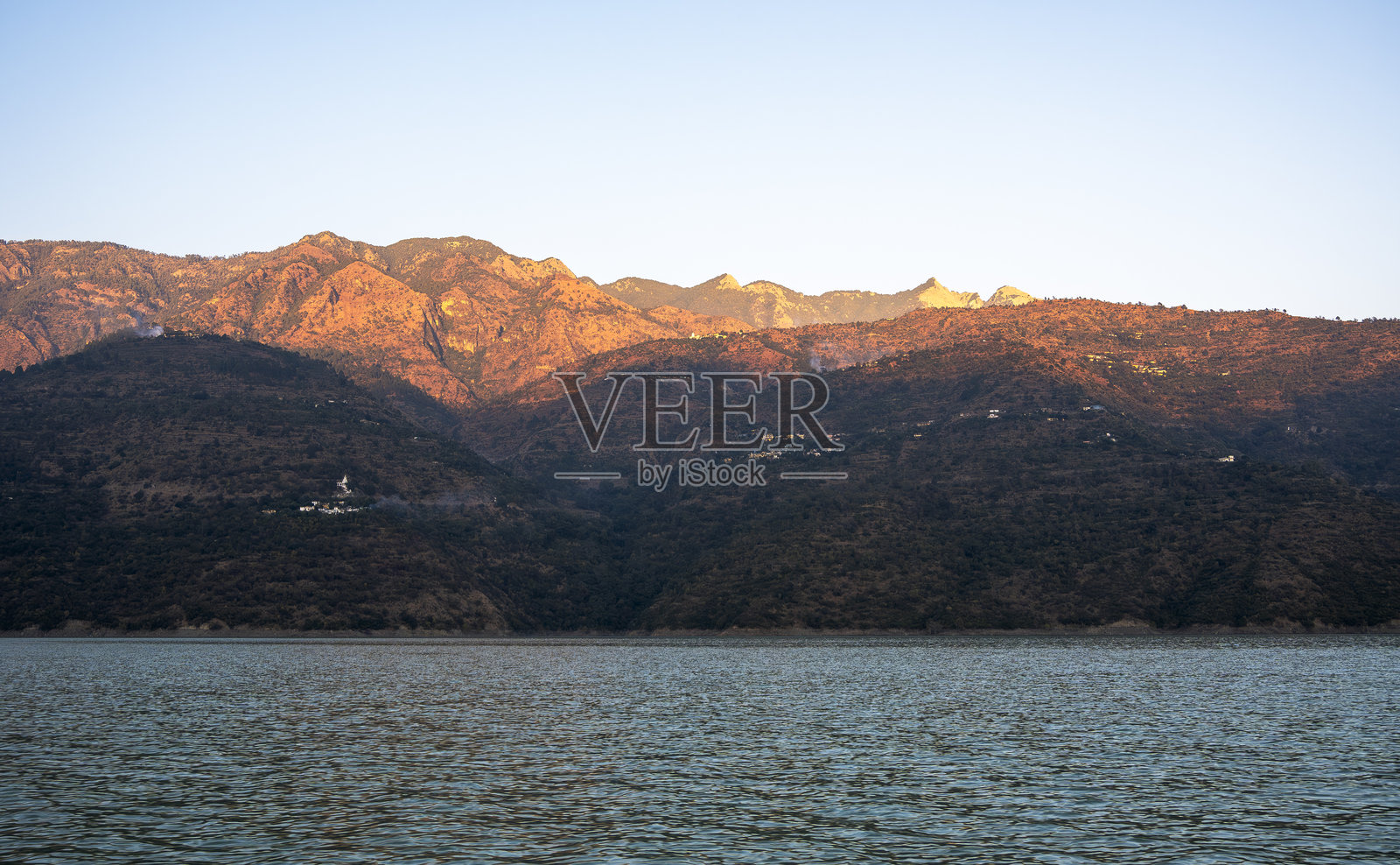 场景捕捉了金色时光下湖面上方的蓝色山脉，平静的水面映照出特赫里湖的壮丽景色。照片摄影图片