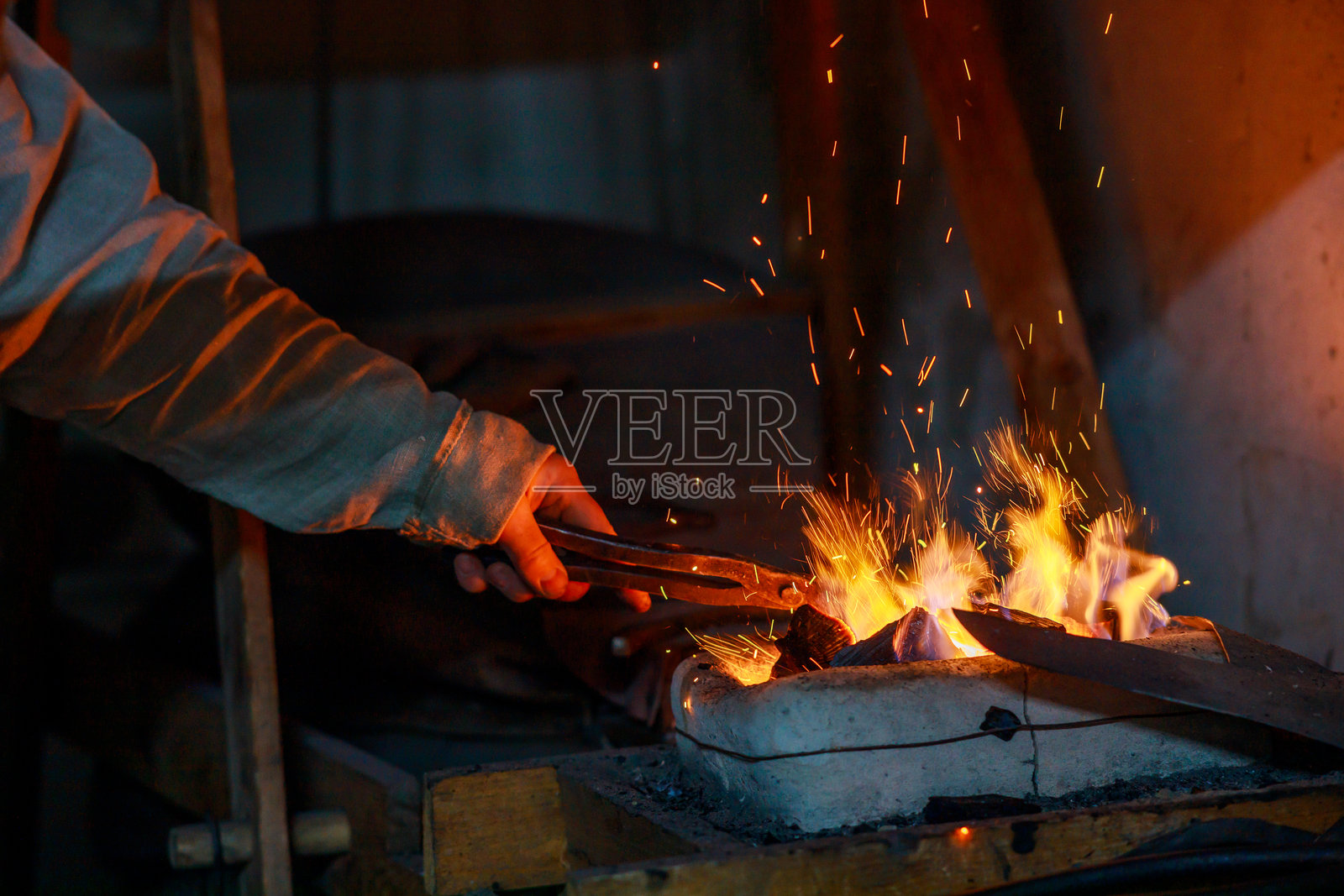 铁匠用钳子夹住一块坯料，悬在炉子上方。照片摄影图片