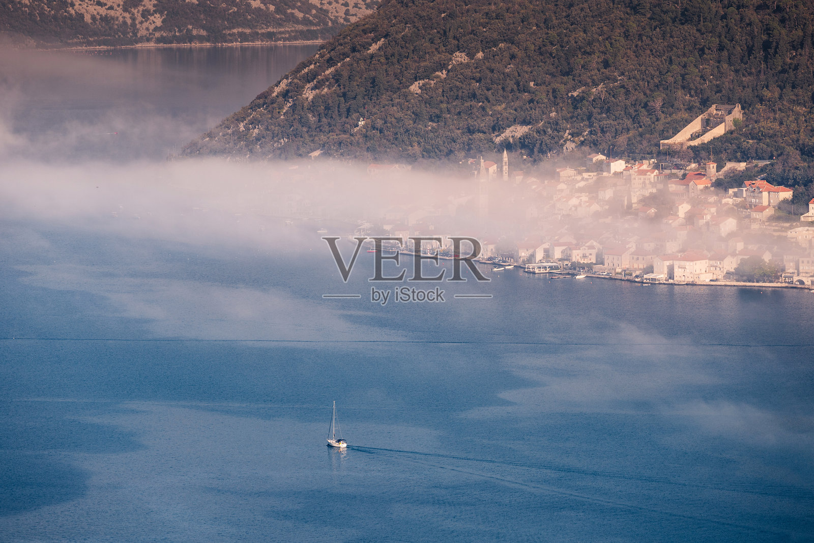 帆船在平静的水面上航行，海岸村庄笼罩在雾中照片摄影图片