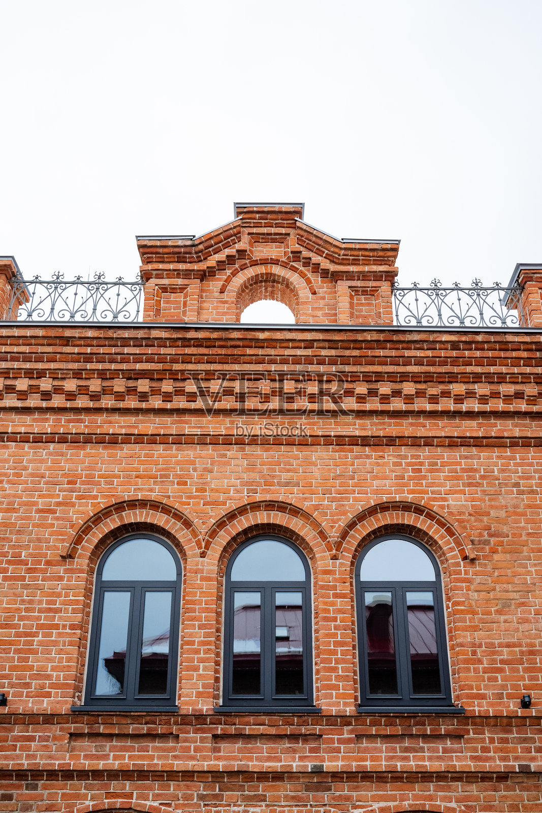 社区里矗立着一座令人惊叹的砖砌建筑，拥有三个优雅的拱形窗户，每个窗户上方都有一个迷人的阳台，展现出精美的建筑细节。照片摄影图片