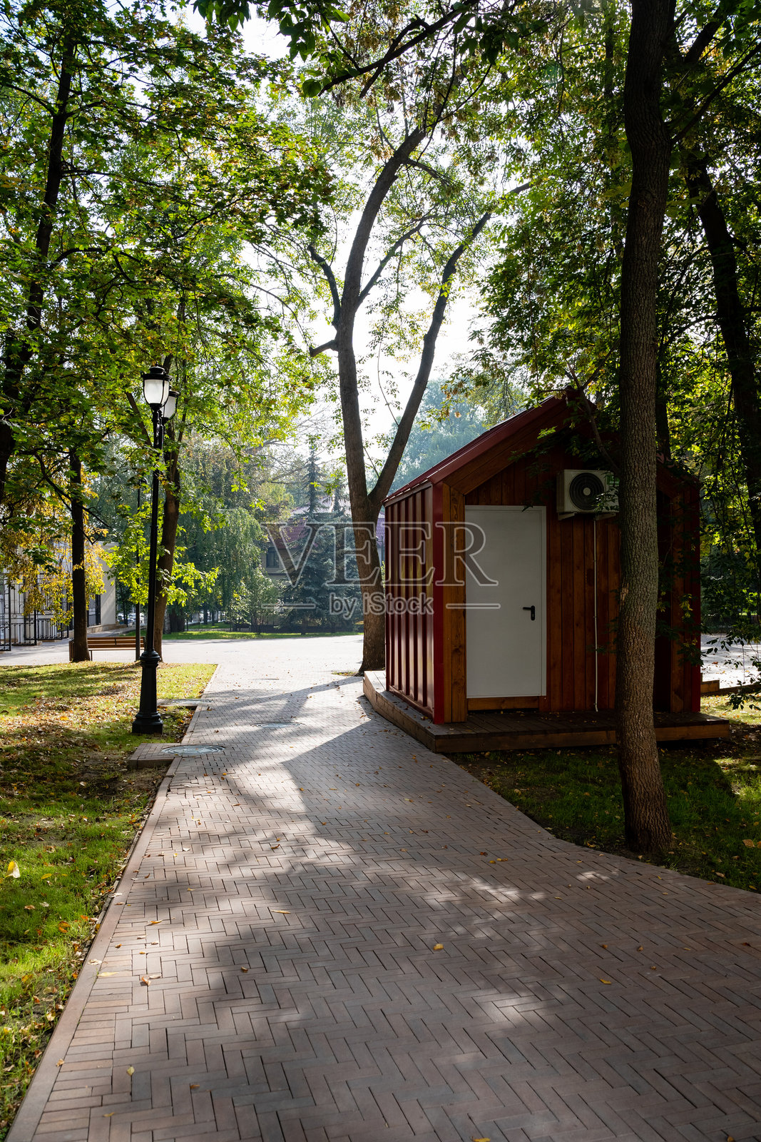 一个迷人而古雅的小木棚美丽地坐落在一条蜿蜒的小径旁，这条小径穿过一个如画的公园，四周被郁郁葱葱的绿意和优美的自然景色环绕。照片摄影图片