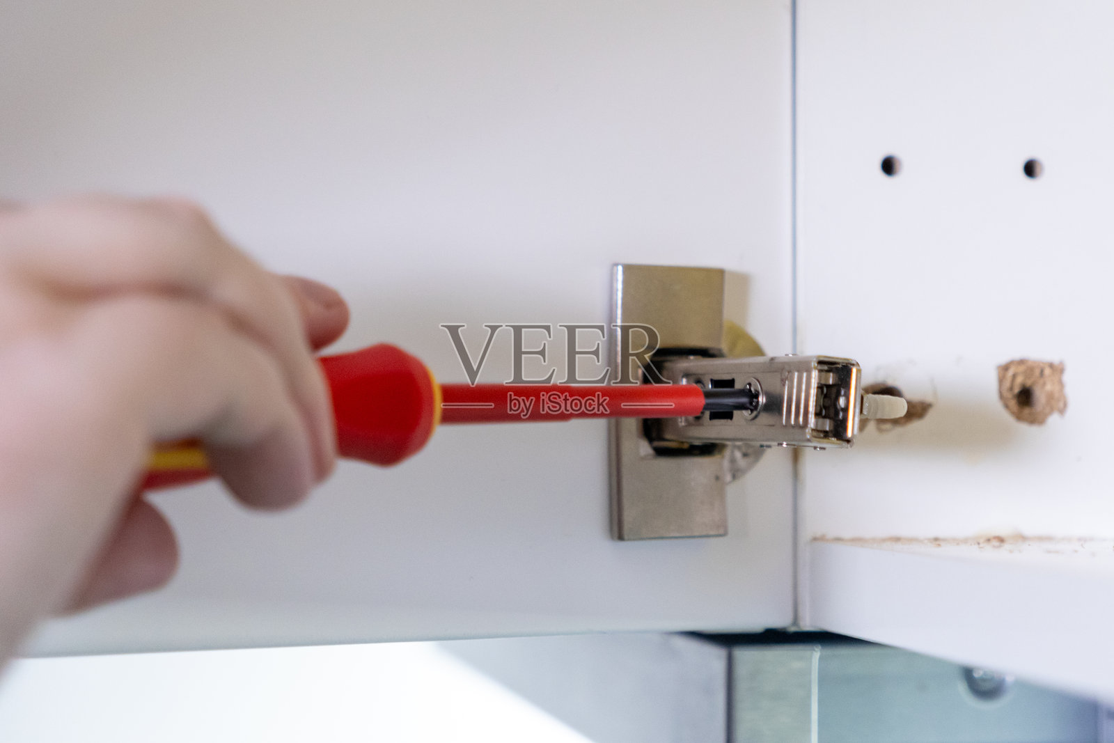 用螺丝刀调整橱柜铰链，以确保门的精确对齐和稳固安装照片摄影图片