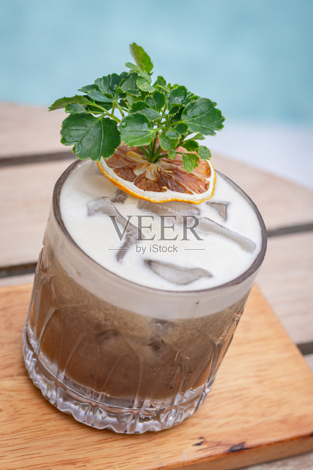 高角度拍摄，清澈的玻璃杯中盛着鸡尾酒，放置在靠近泳池的木质表面上照片摄影图片