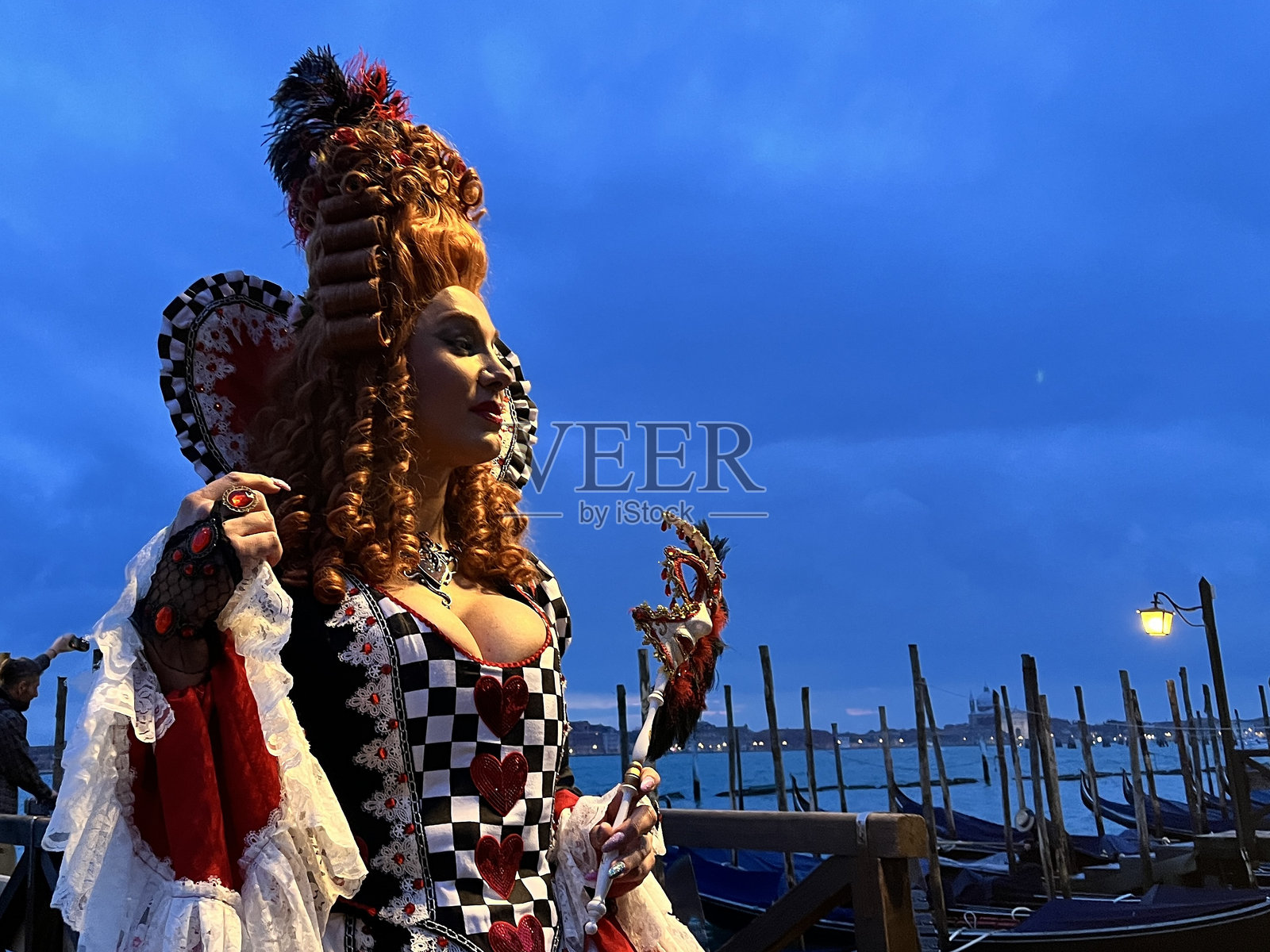 穿着红心女王服装的女性在日落时分于威尼斯摆姿势照片摄影图片