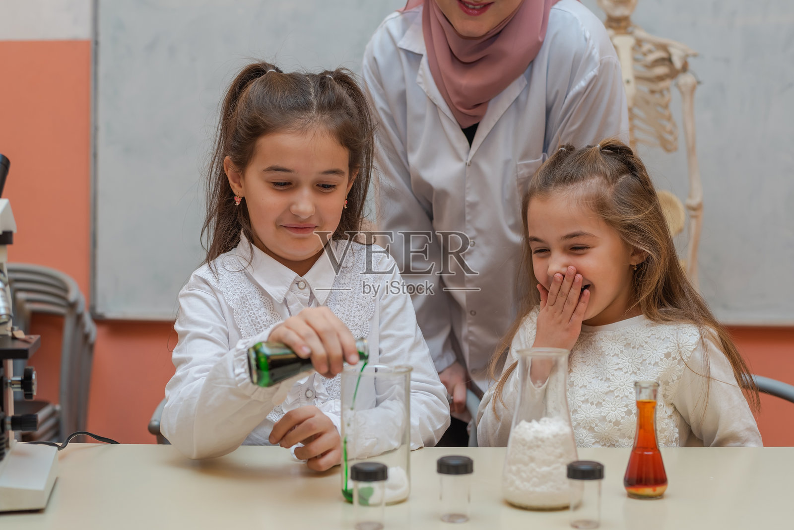 孩子们和一位女性穆斯林老师在学校实验室进行化学科学实验。照片摄影图片