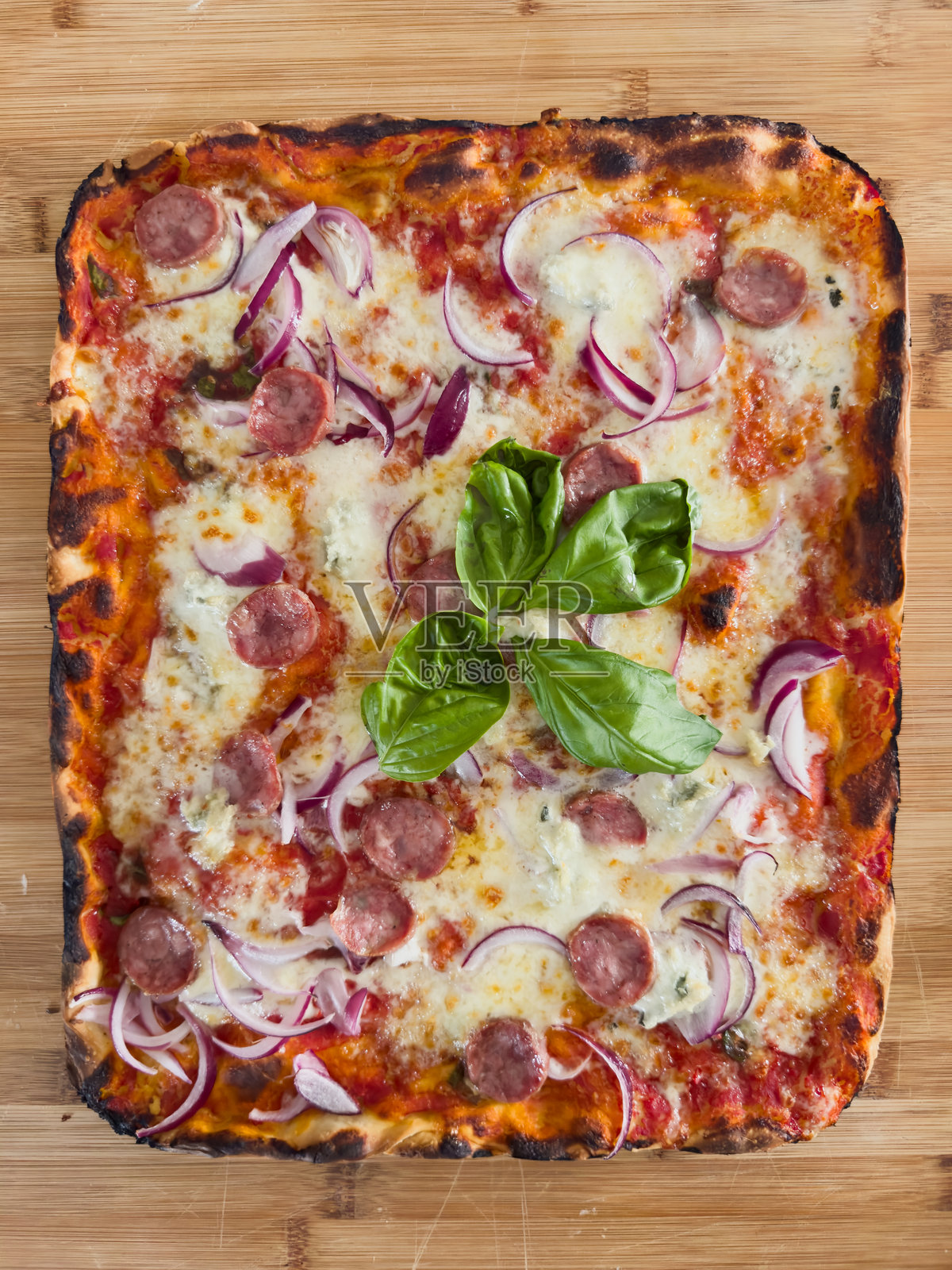 美味的方形披萨，上面有特罗佩亚红洋葱、戈贡佐拉奶酪和香肠，放在切菜板上照片摄影图片