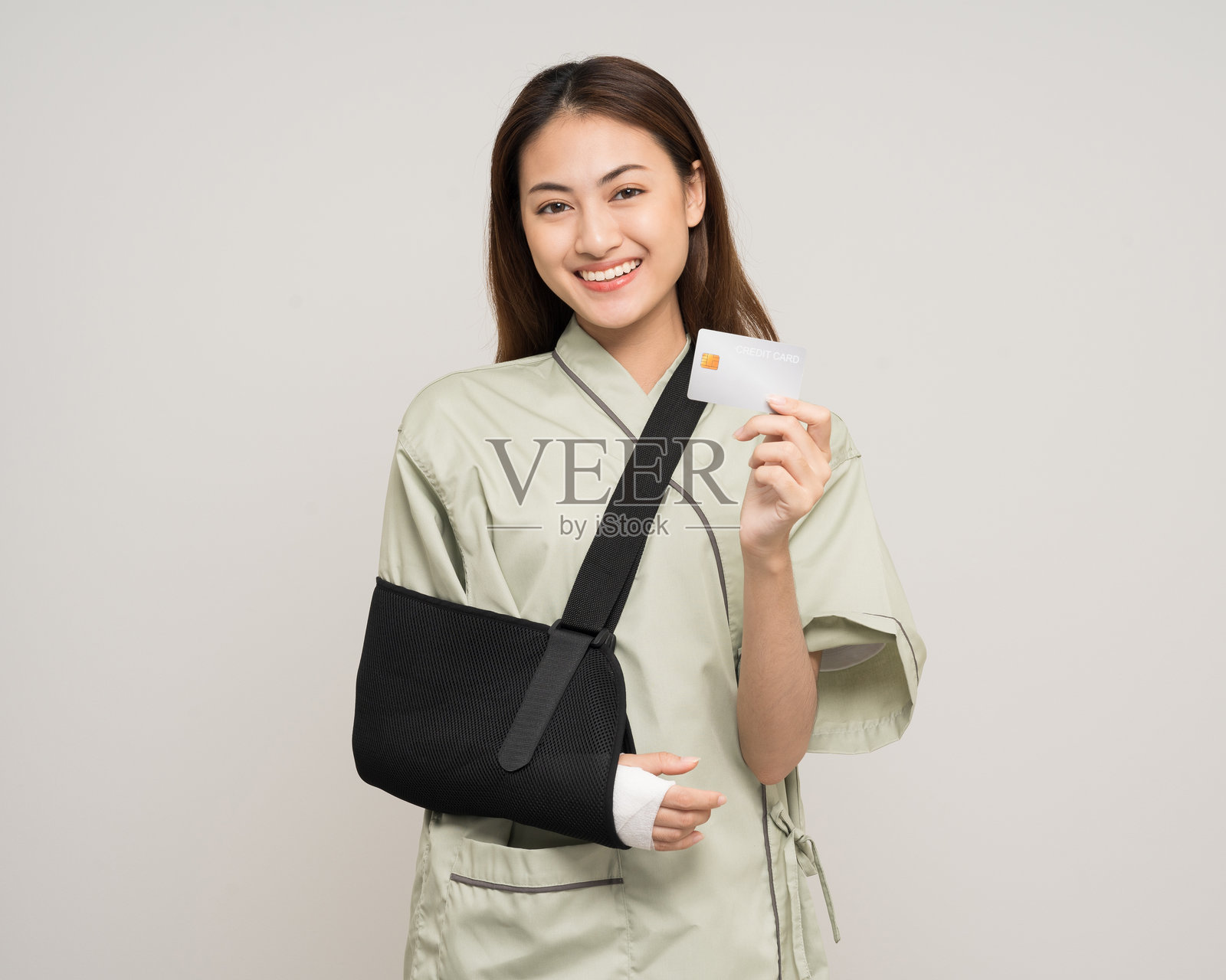 亚洲女性手臂和腿部骨折，手持信用卡进行支付。女性佩戴石膏夹板，患者佩戴吊带支撑手臂，涉及人寿保险和意外事故。照片摄影图片