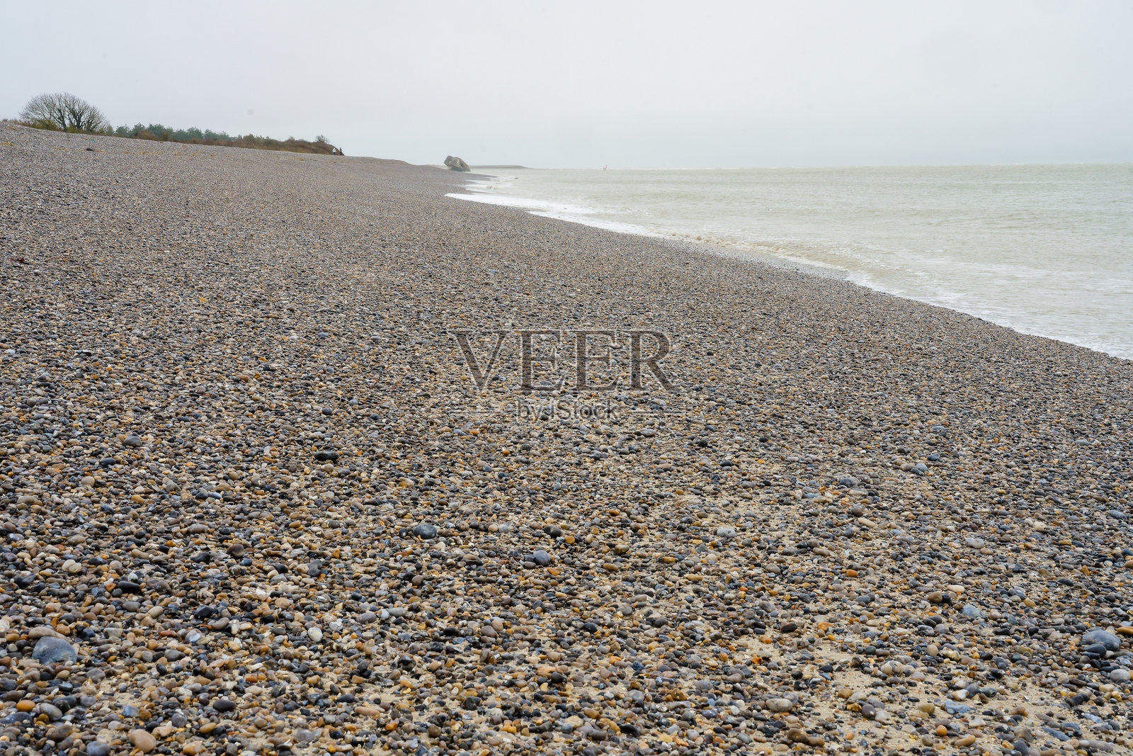 岩石海滩的海岸线，铺满卵石，阴云密布的天空，水边的宁静日子照片摄影图片