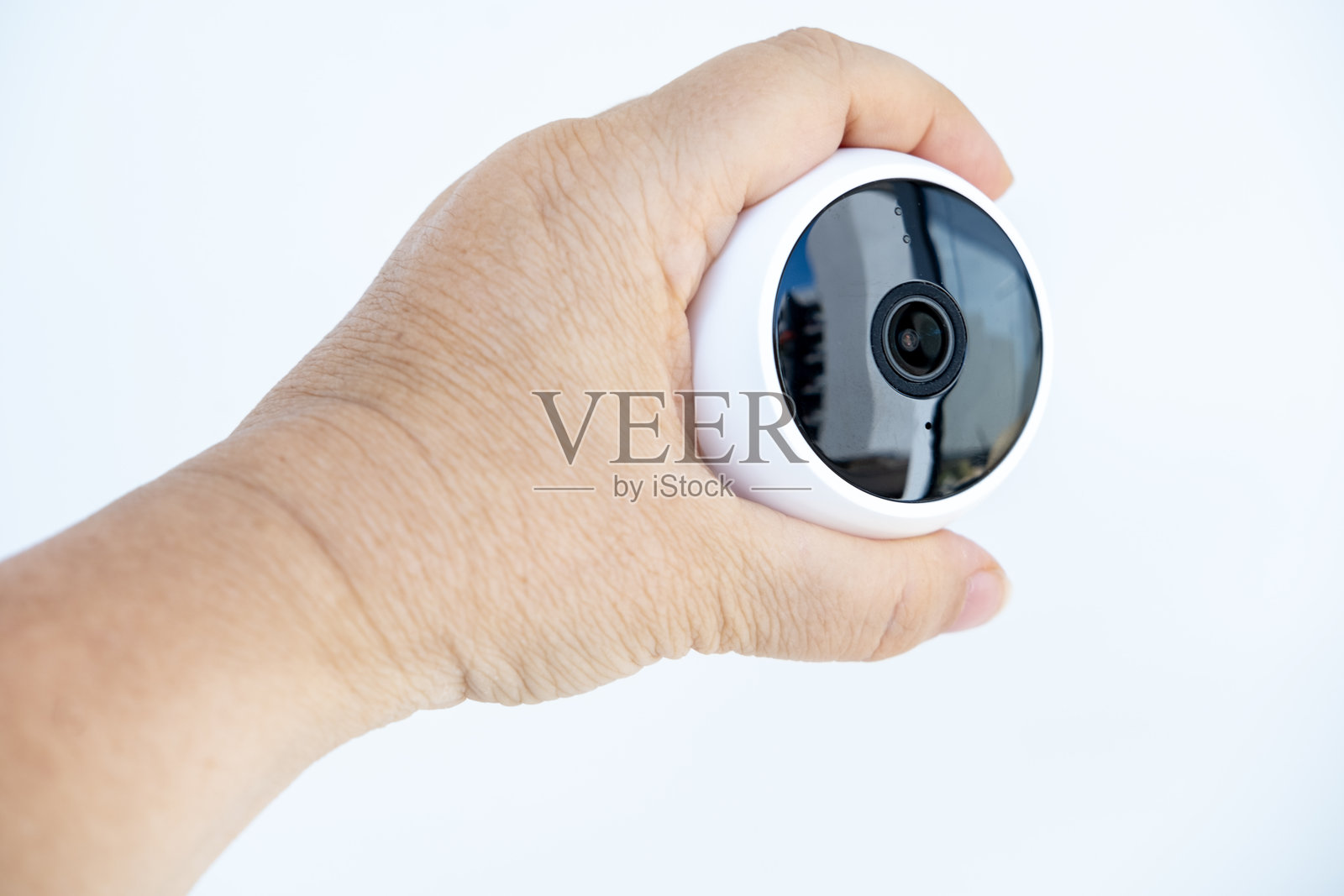 一个人手持紧凑型、现代化、球形的小型安防摄像头，设计流畅，背景为白色，现代家居安防解决方案照片摄影图片