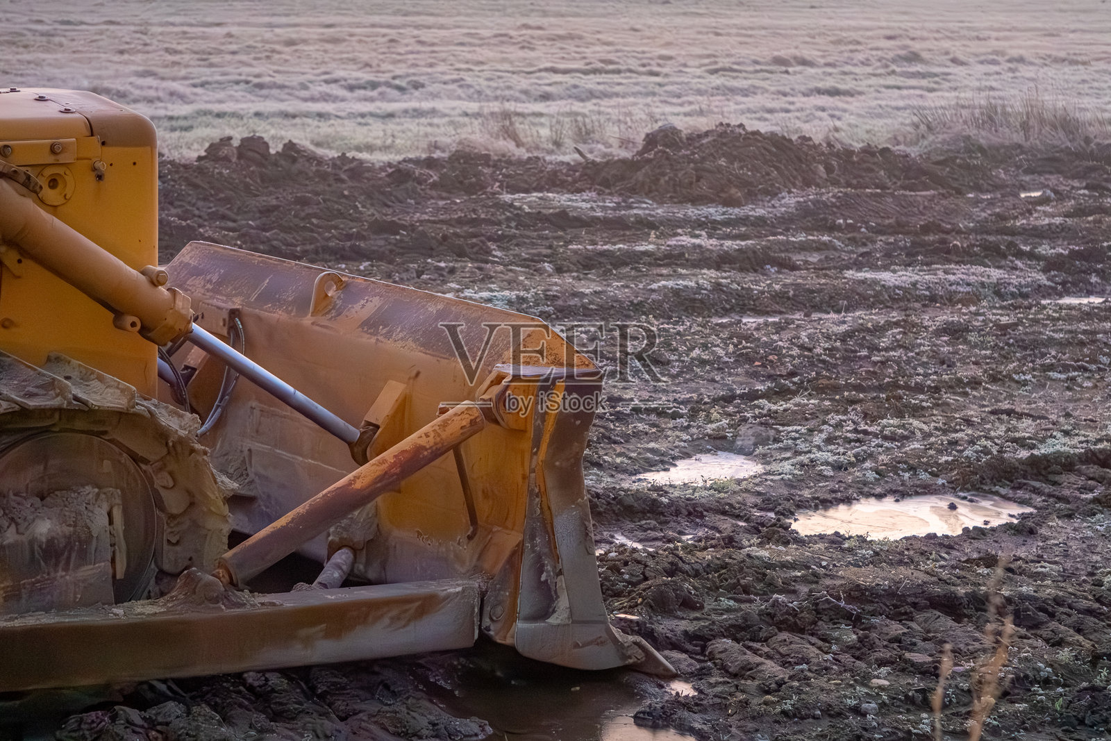 旧的毛毛虫推土机在新公司的施工现场。冬季寒冷的早晨，施工机器在泥泞的田野中。照片摄影图片