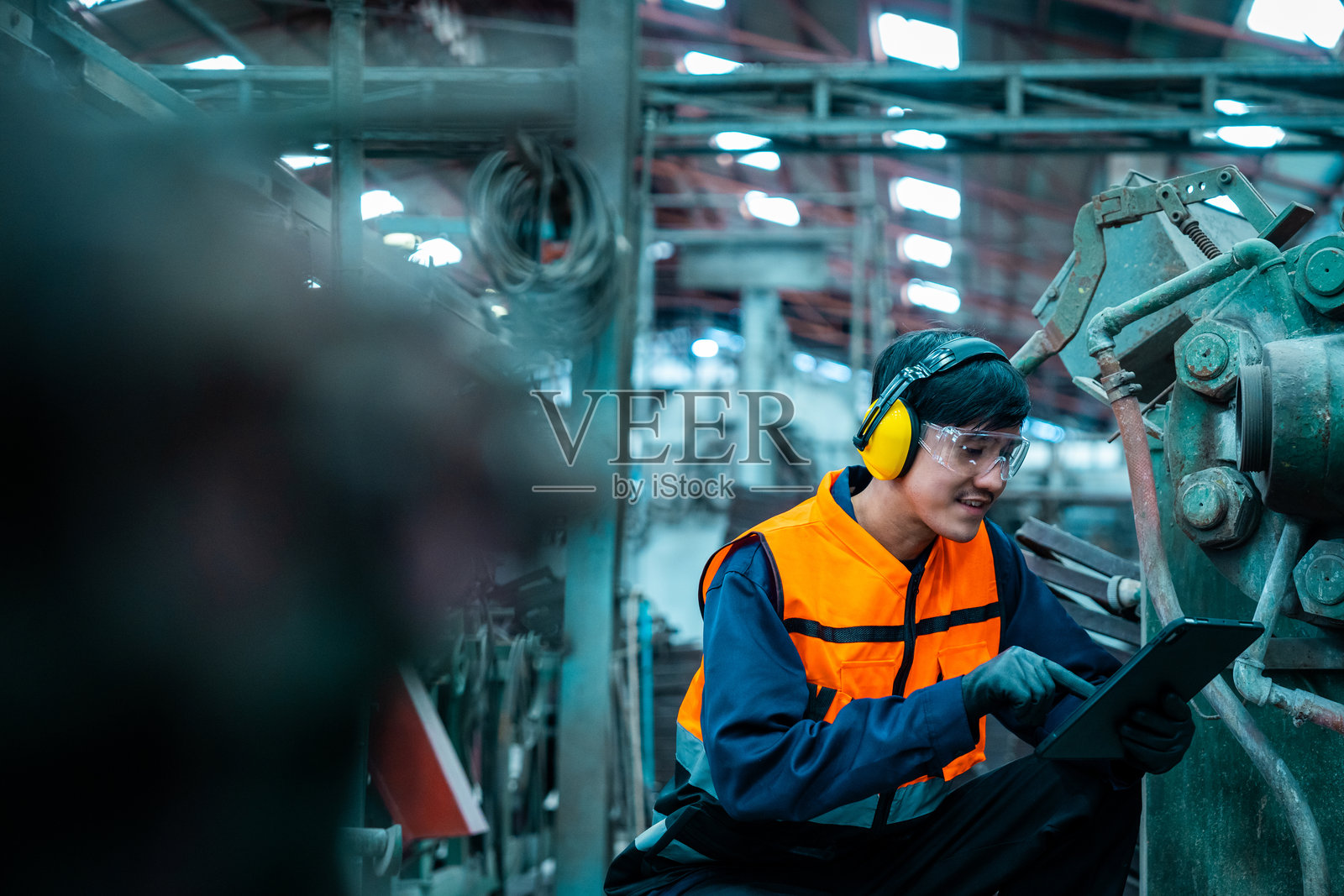 自信的工程师戴着安全头盔，站着用平板电脑在工厂仓库中进行分析。亚洲技术人员在工业工厂进行设备检查和控制。照片摄影图片