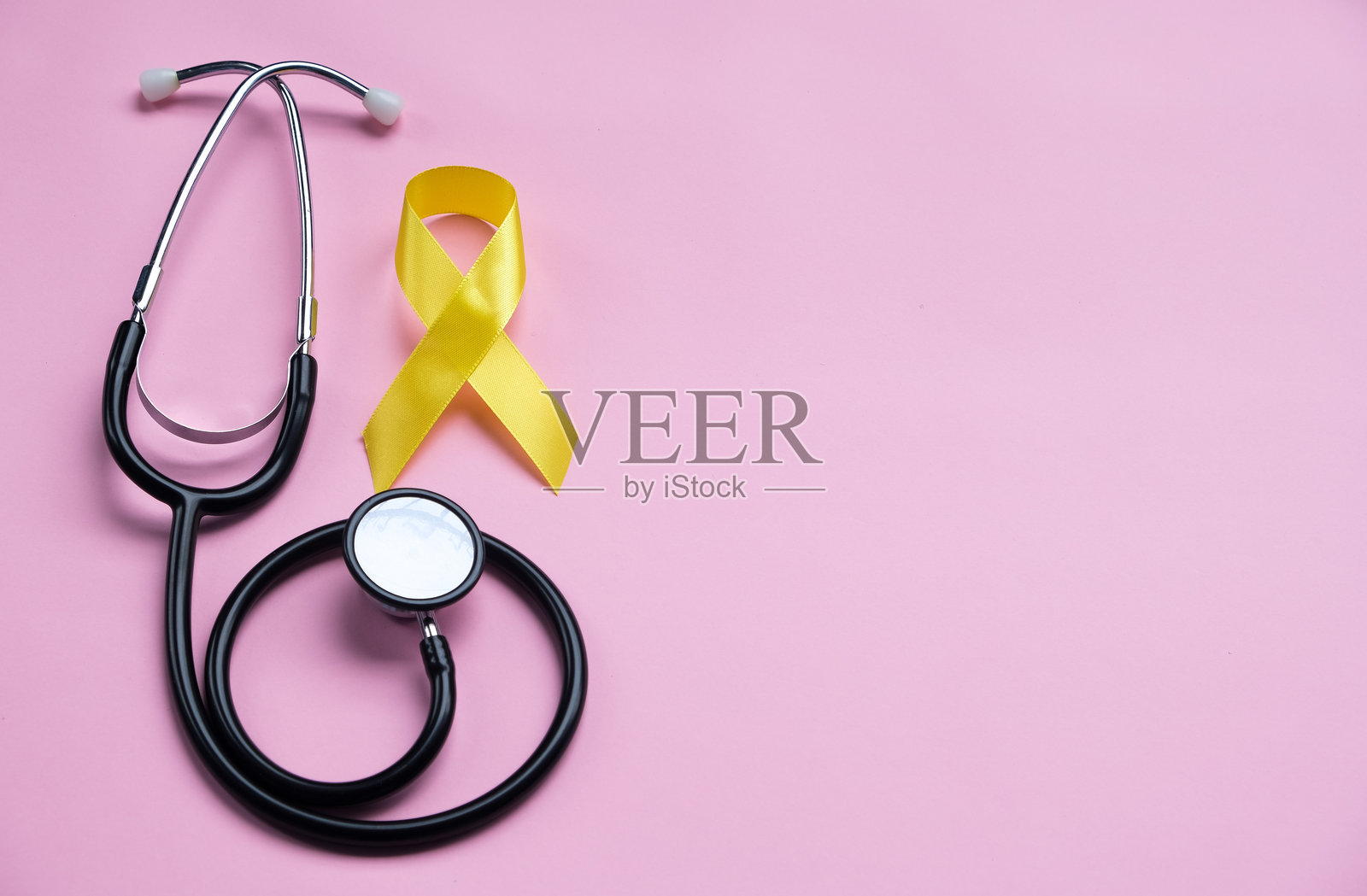 粉色背景上的黄色丝带与听诊器。儿童癌症意识概念照片摄影图片
