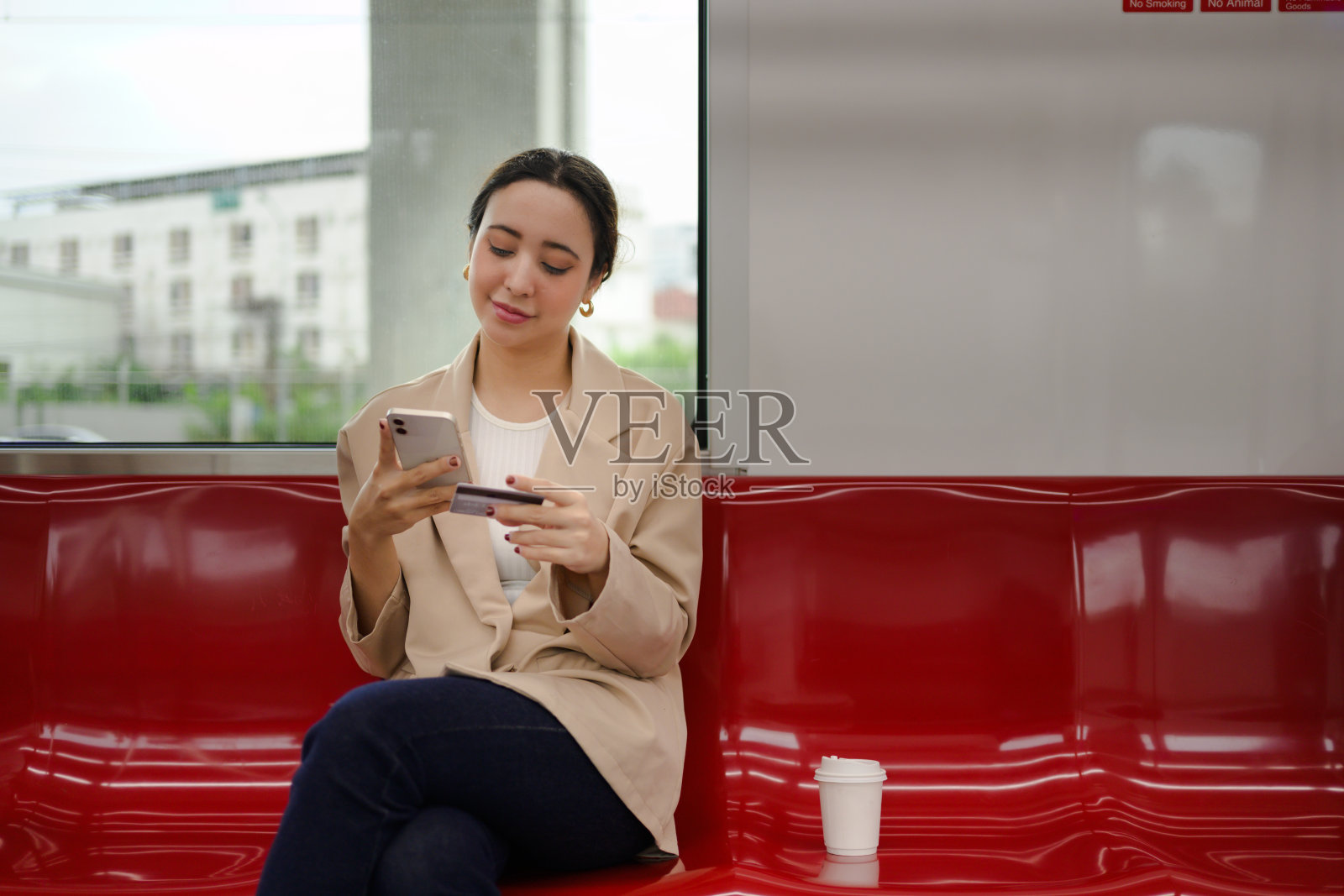 年轻女商人在地铁上通勤时，使用智能手机和信用卡进行在线购物，同时享受咖啡。照片摄影图片