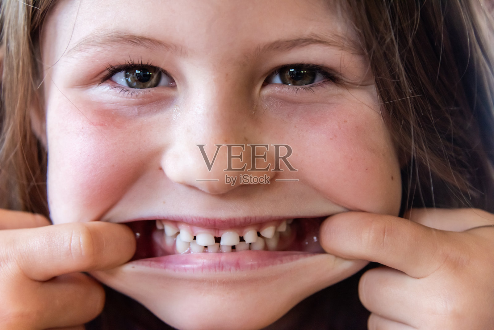 白人漂亮的小女孩对着镜头微笑，做鬼脸露出牙齿。照片摄影图片