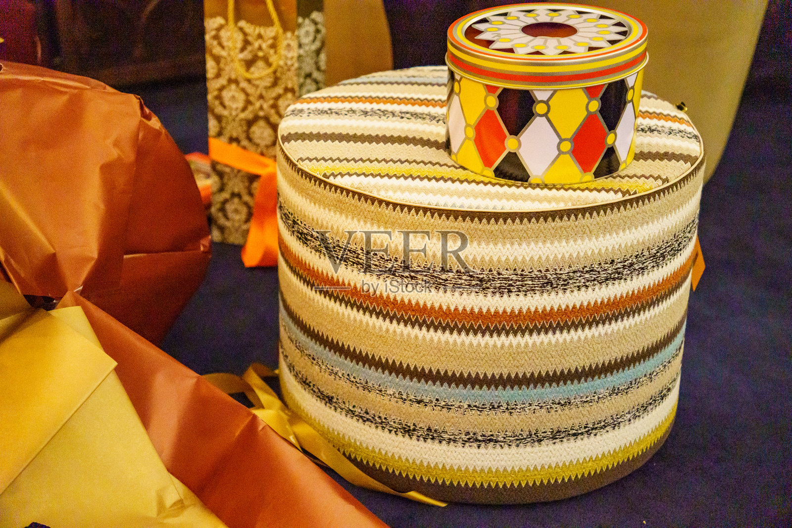 一个多色的圆形凳子（坐垫），表面覆盖着锯齿形图案的布料，上面放着一个颜色协调的罐子。照片摄影图片