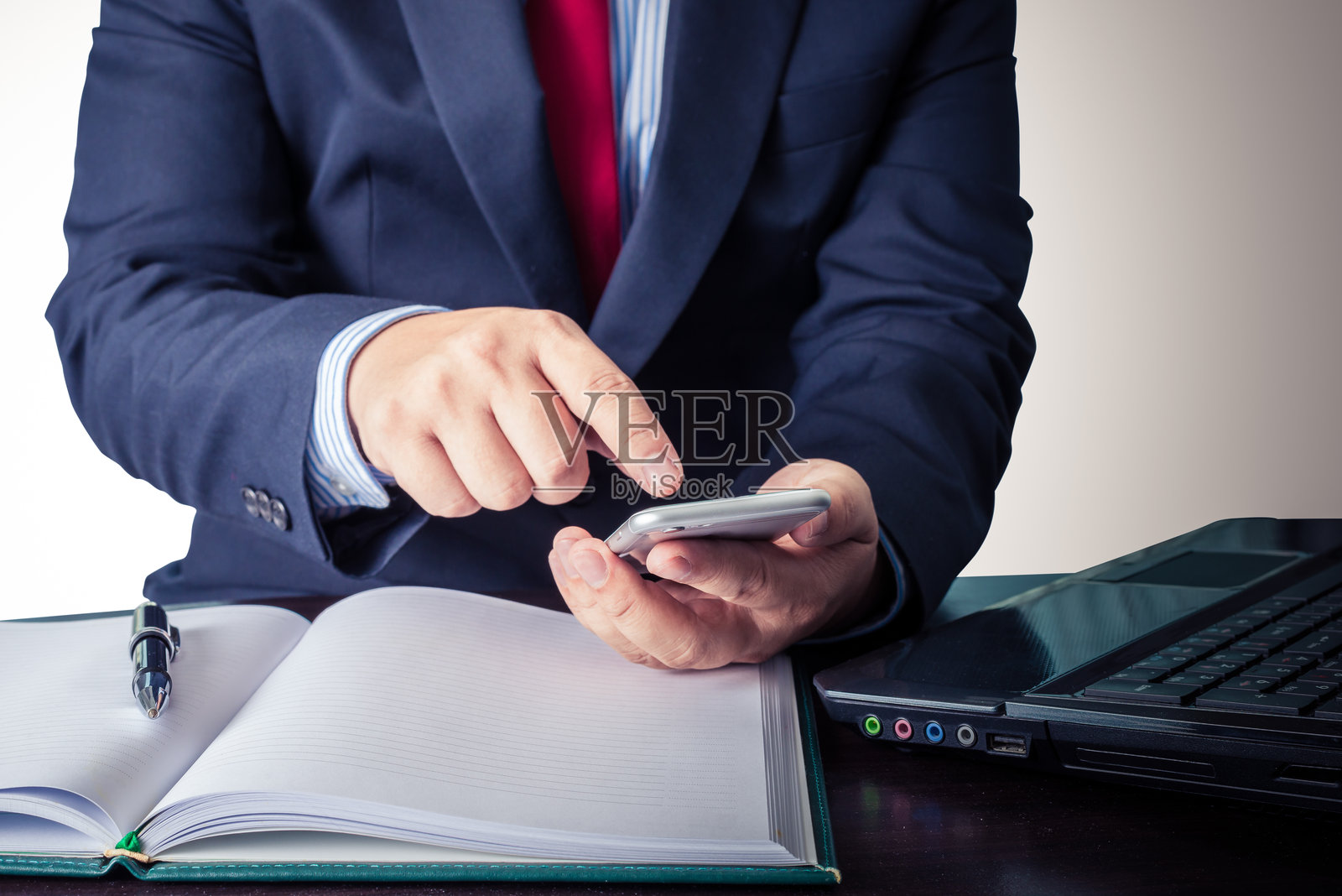 商人坐在桌子前使用手机的中部特写照片摄影图片