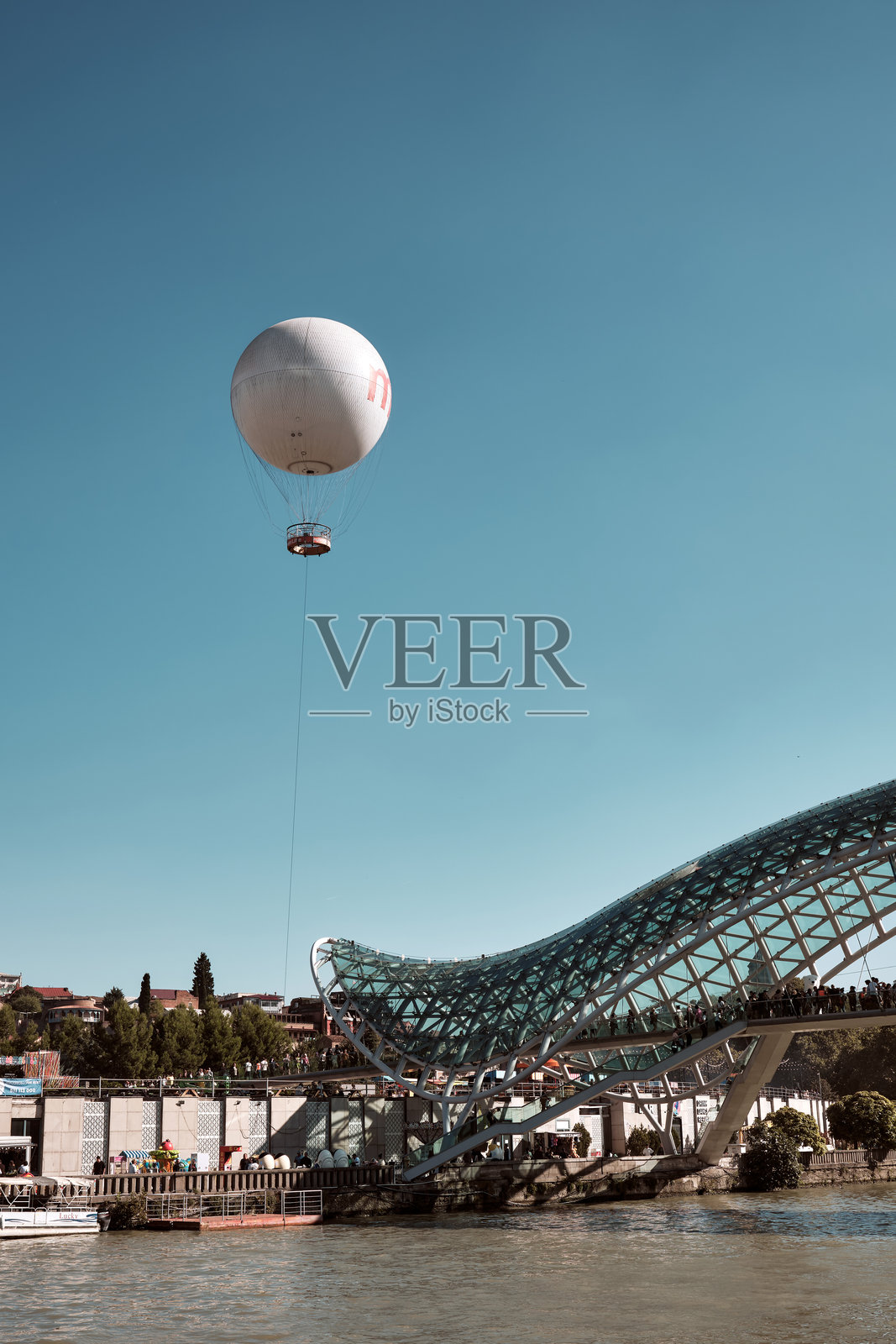 美丽的步行桥,玻璃屋顶覆盖在库拉河上。和平桥和受欢迎的旅游景点热气球。照片摄影图片