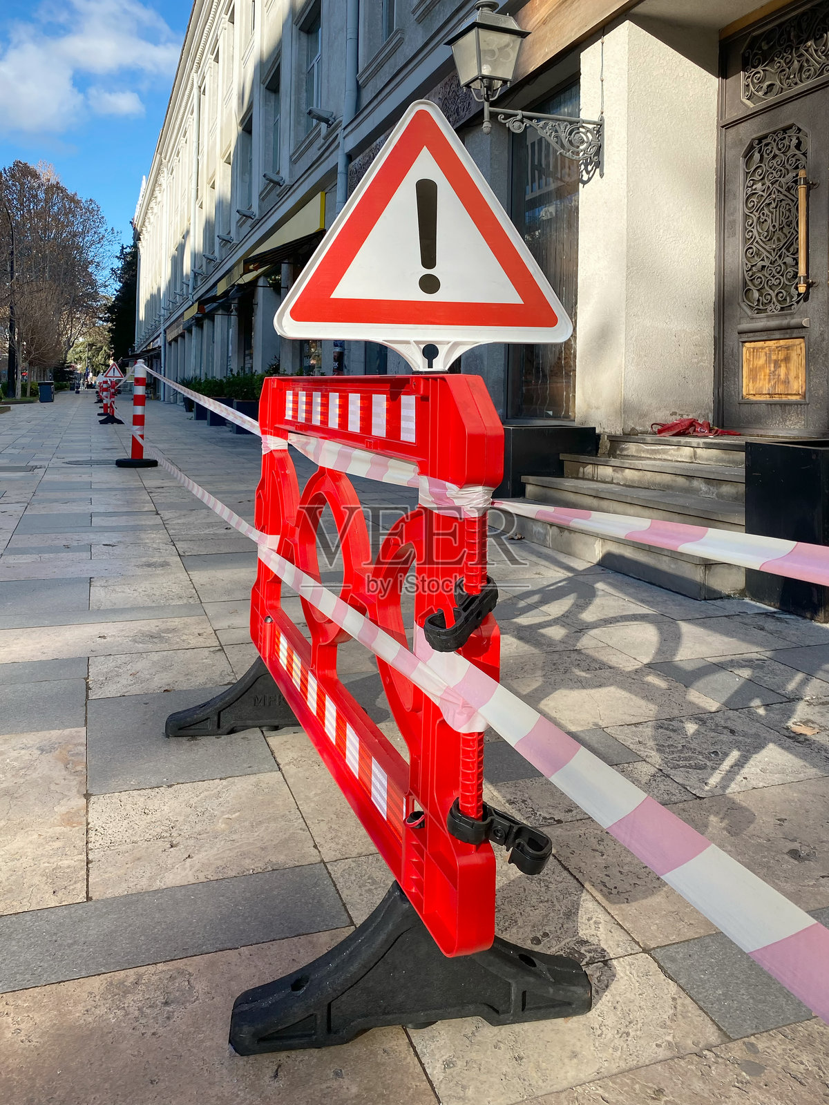 竖直的红色障碍物，上面拉着塑料带。火灾后禁止进入建筑。照片摄影图片