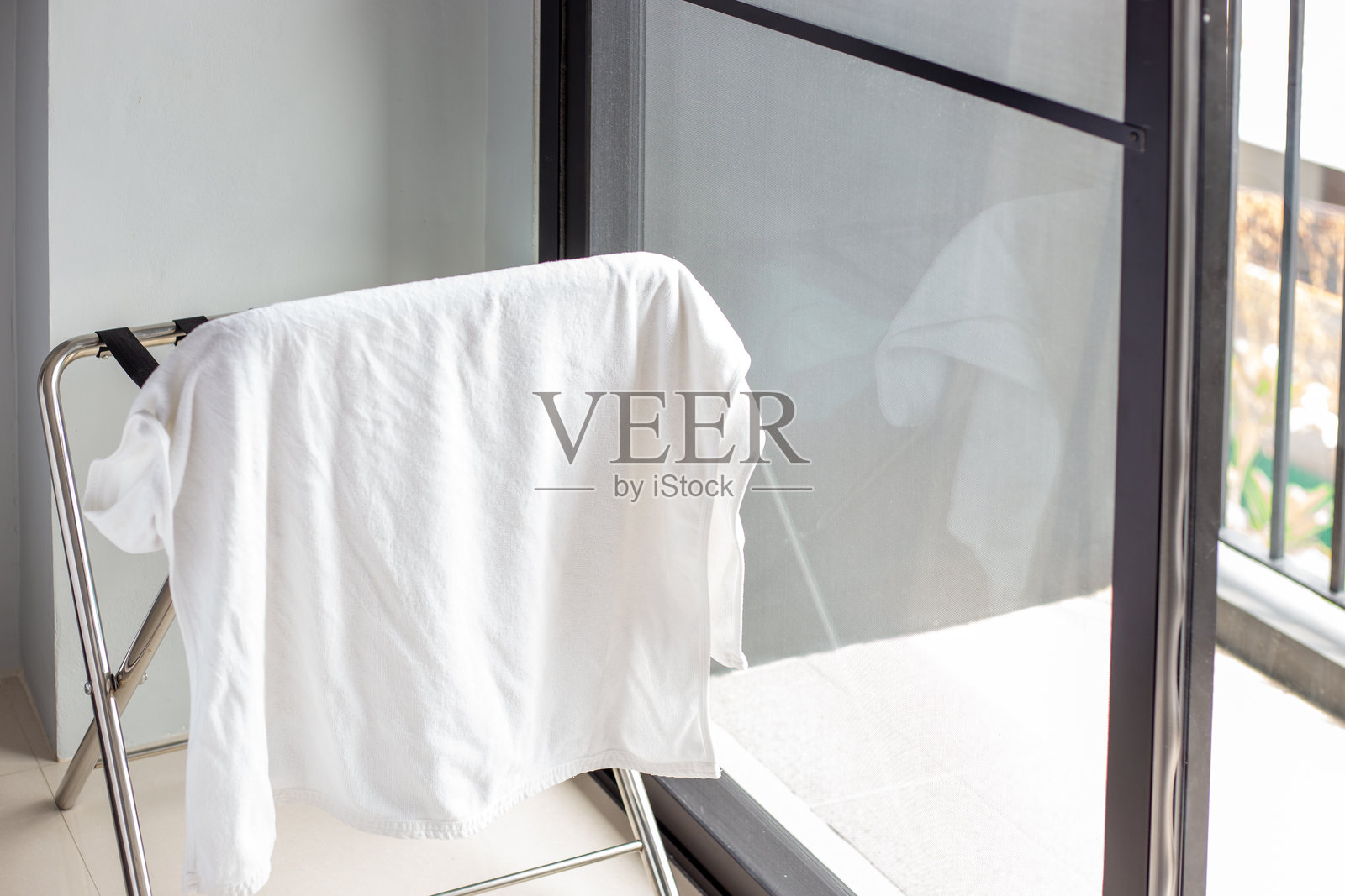 带有悬挂白色毛巾的折叠晾衣架，房间内有大窗户和阳台。室内设施与环境。照片摄影图片